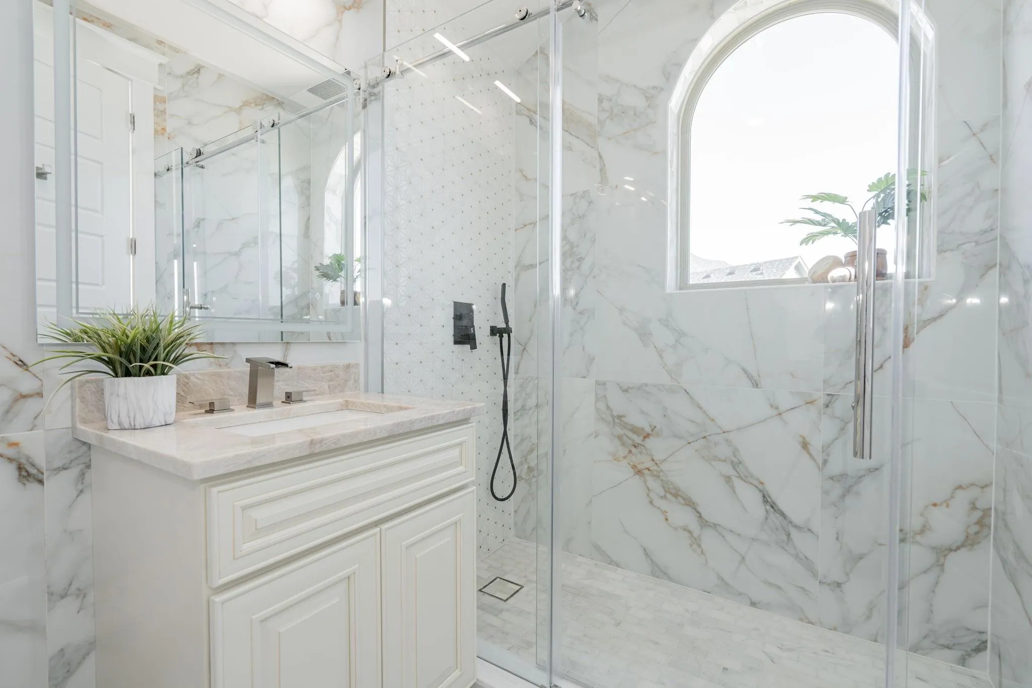 Bathroom featuring a glass-enclosed shower with an arched window, full-height marble-look tile, a single vanity with a light-toned countertop, and a mirrored medicine cabinet