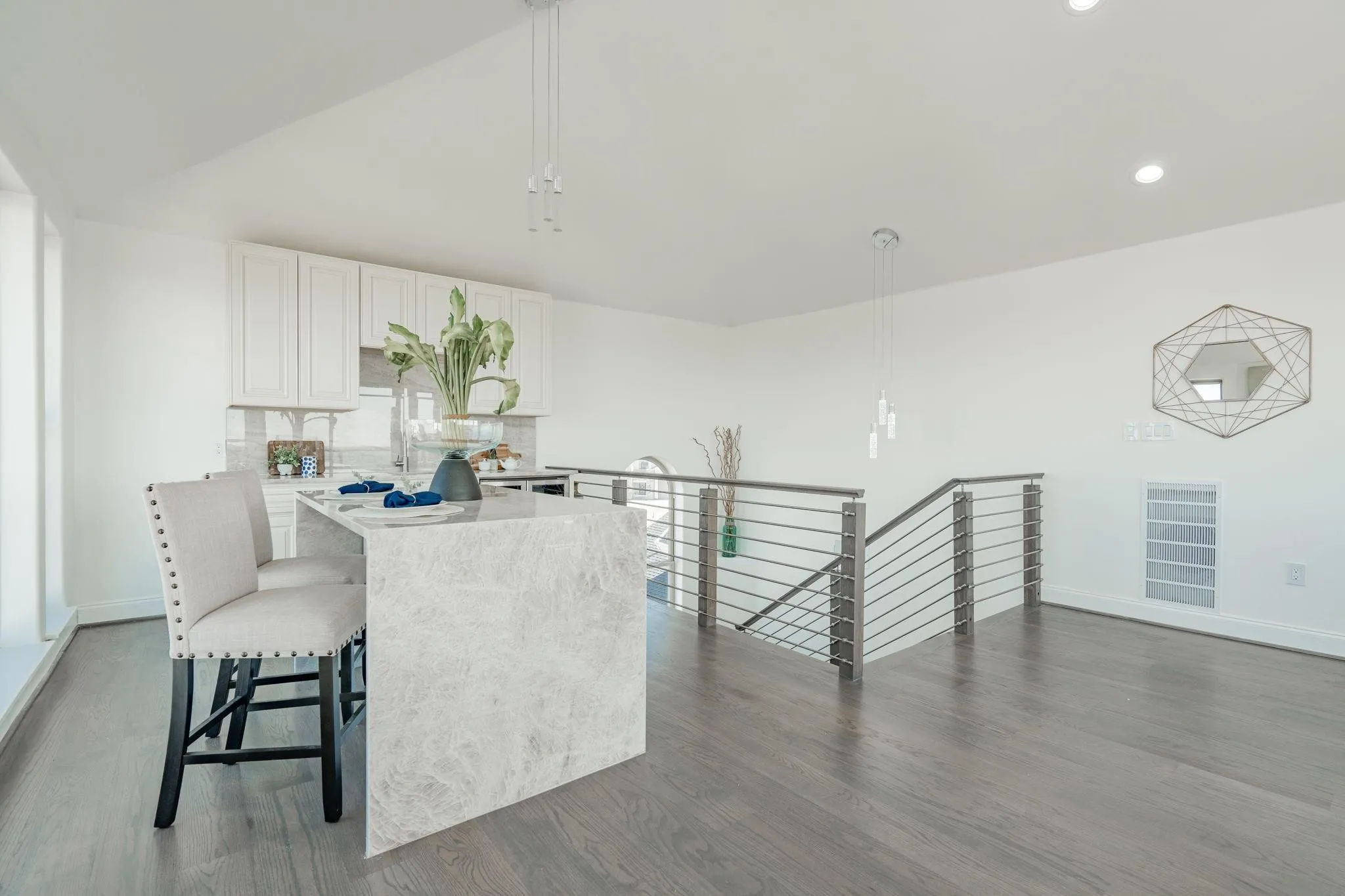Open-concept living area featuring an eat-at kitchen island with waterfall countertop, stainless steel cable railing, recessed lighting, and wood-finish flooring