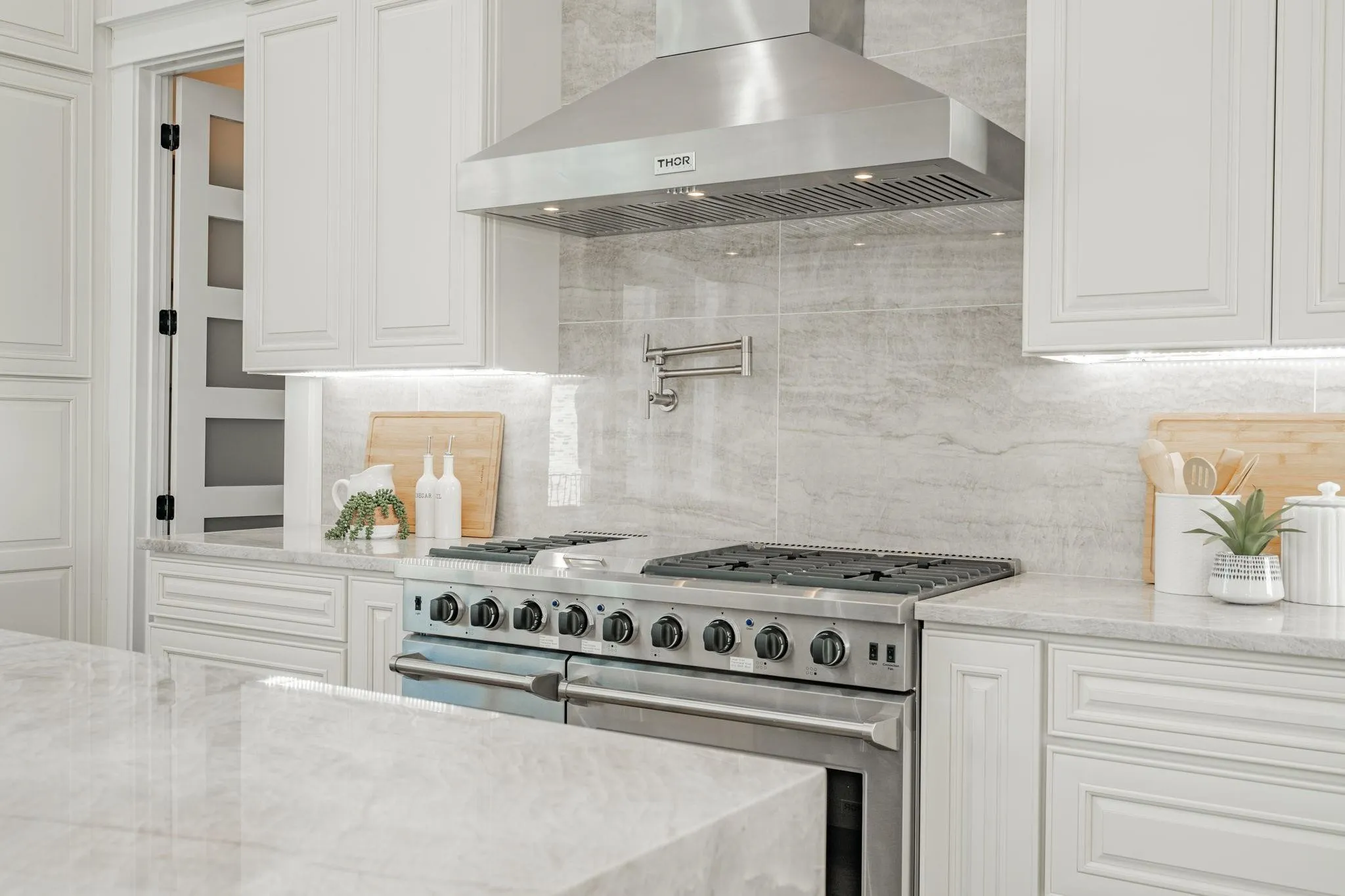 Gourmet kitchen featuring a stainless steel range with a pot filler, coordinating range hood, white cabinetry, and stone countertops