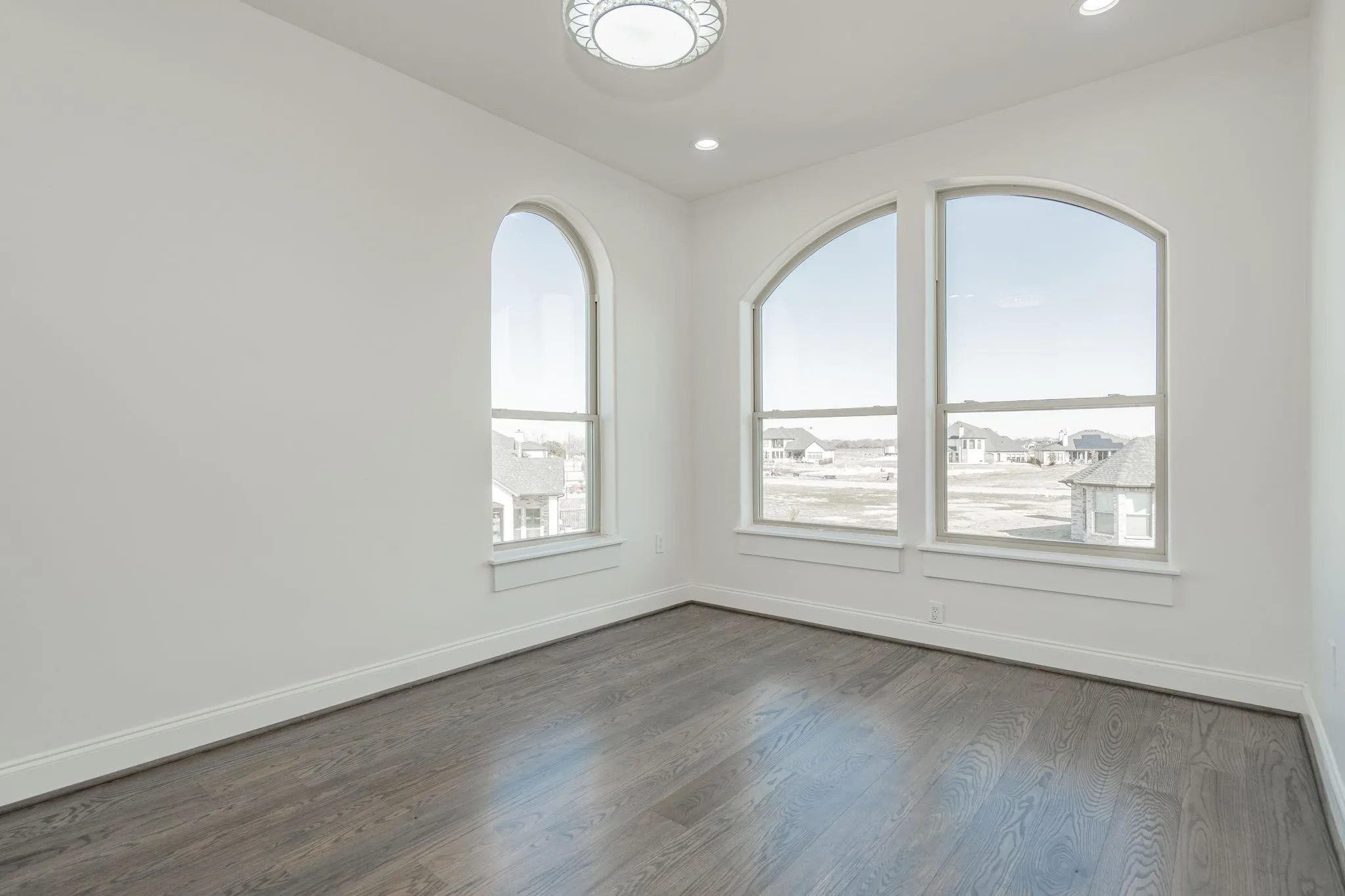 Room featuring three arched windows, wood-finish flooring, white walls, recessed lighting, and a decorative ceiling light fixture