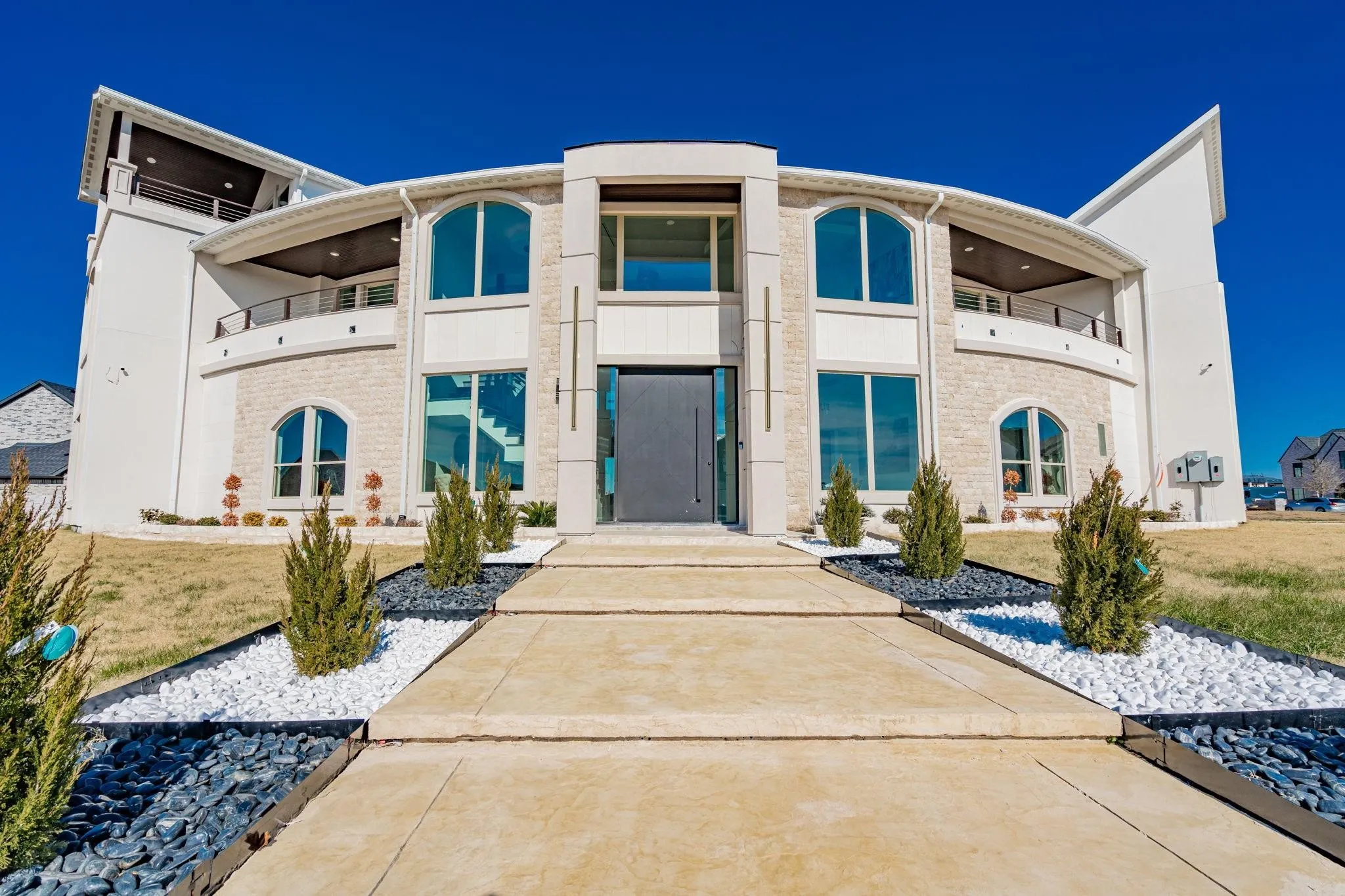 Modern architectural exterior featuring a prominent arched entrance, stone façade accents, and an upper-level balcony