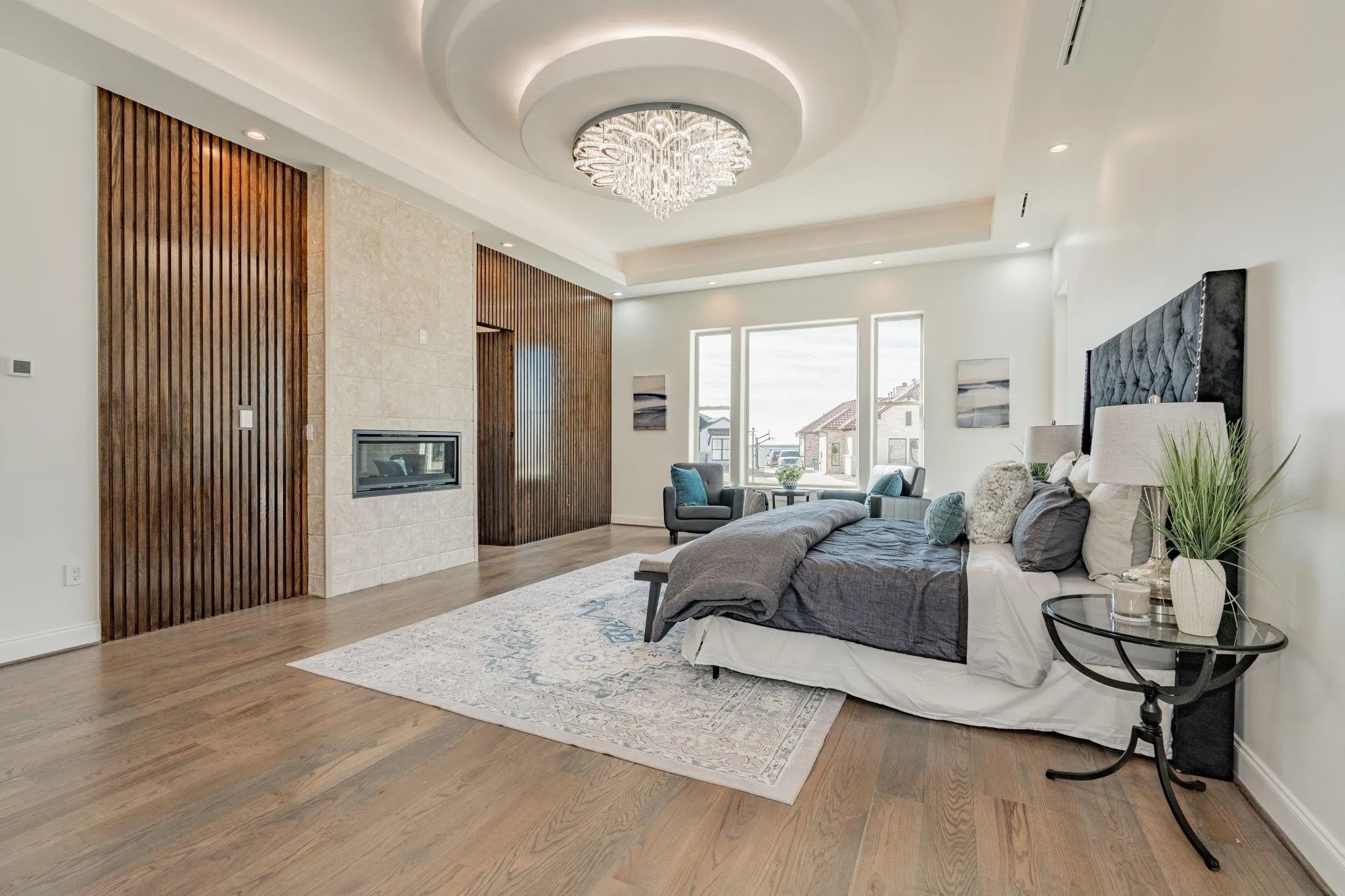 Spacious room featuring wood-finish flooring, a built-in fireplace with stone-look surround, a decorative chandelier, and multiple large windows