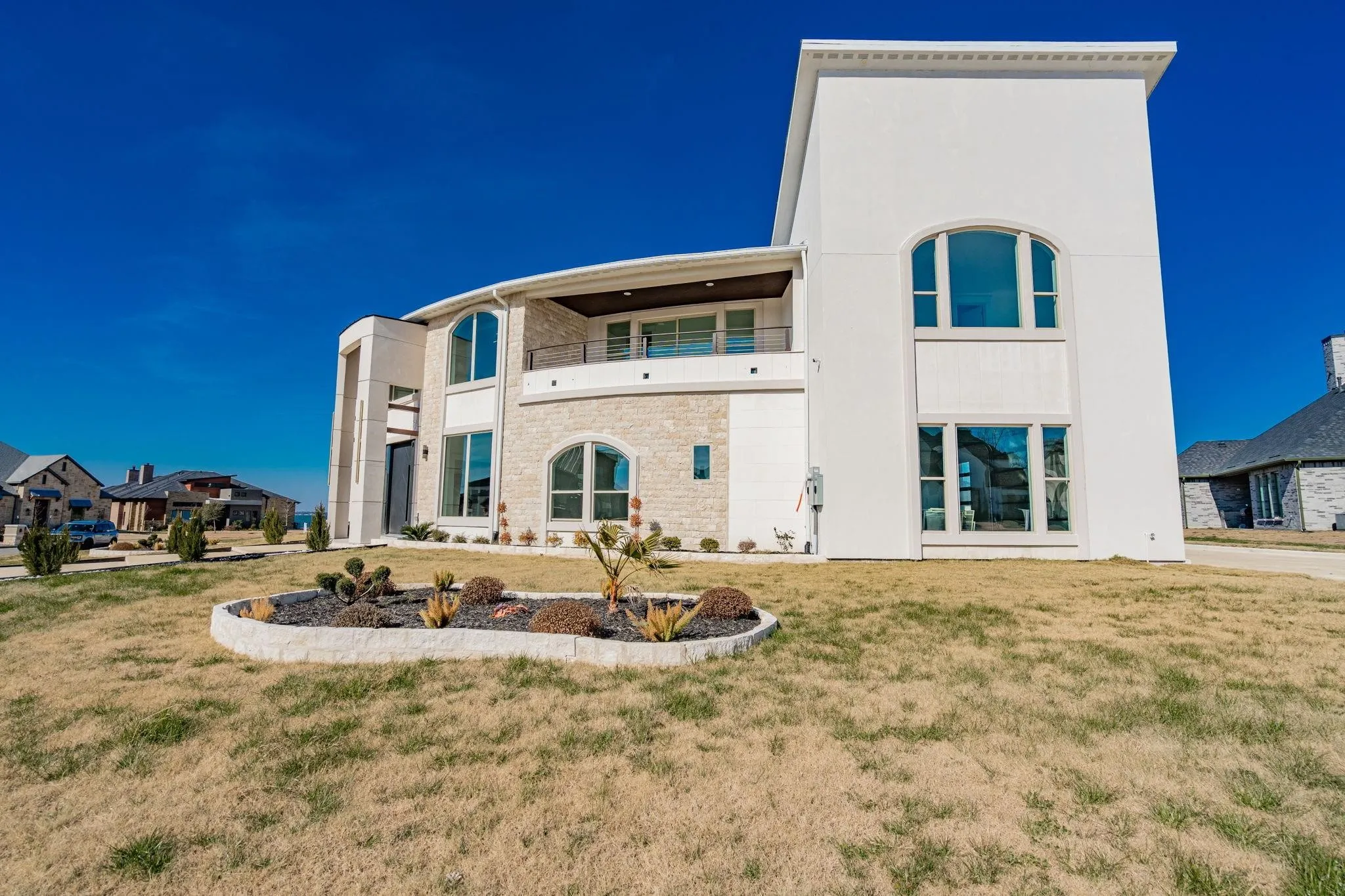 Contemporary white stucco exterior featuring stone accents and a prominent two-story arched window