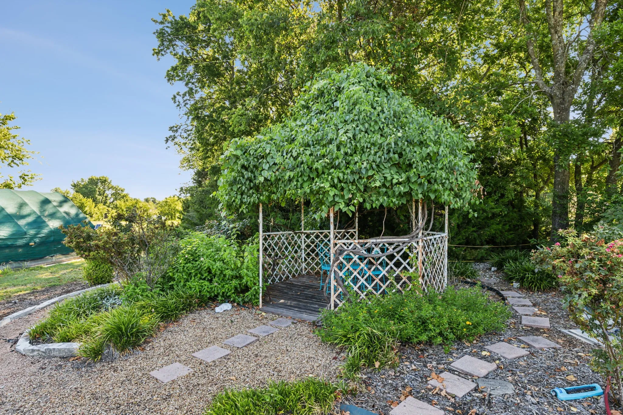 Landscaped garden area featuring a white latticework gazebo with a natural leafy canopy
