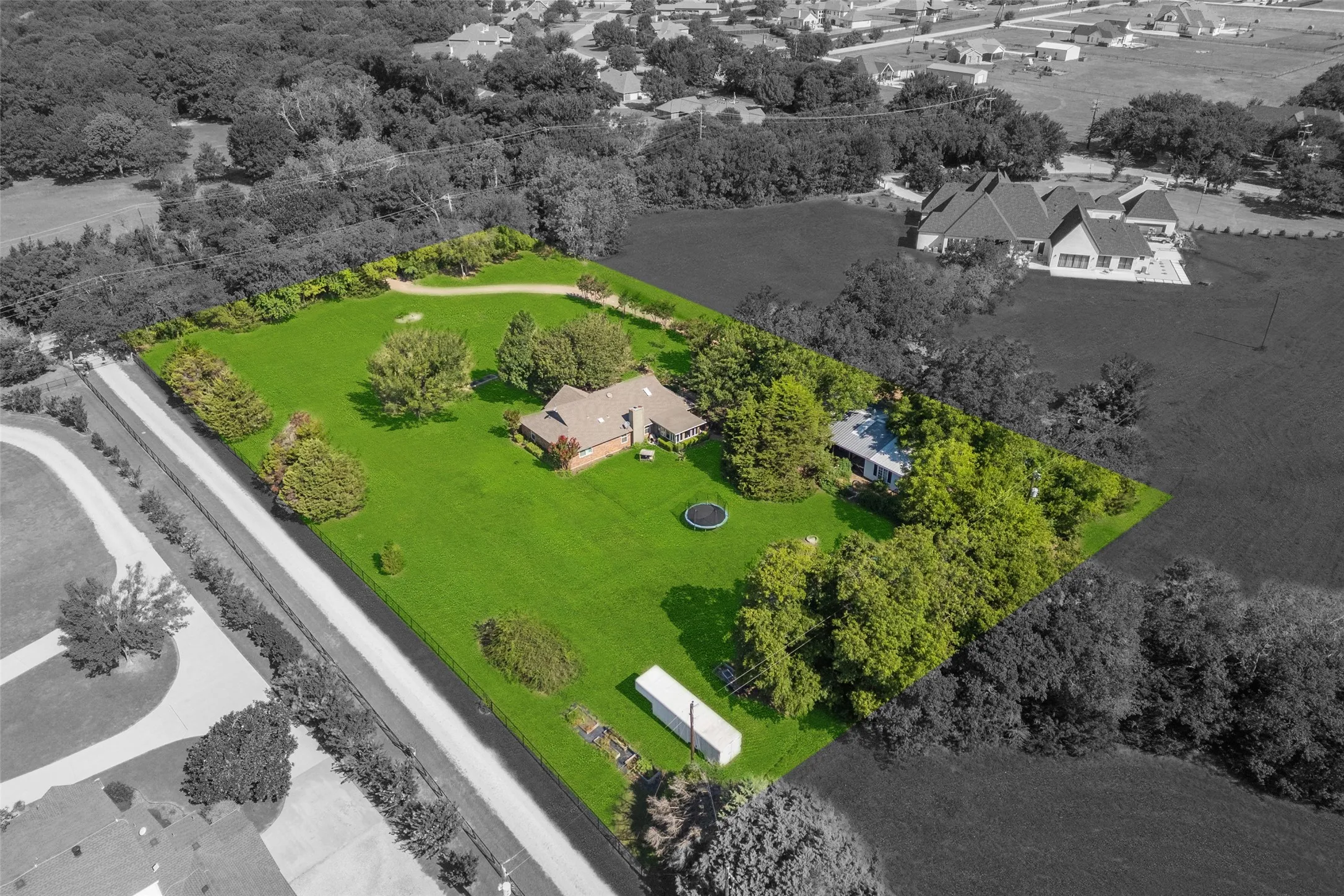 Expansive green lawn surrounds a brick and shingle-roof residence, featuring mature trees and a private driveway