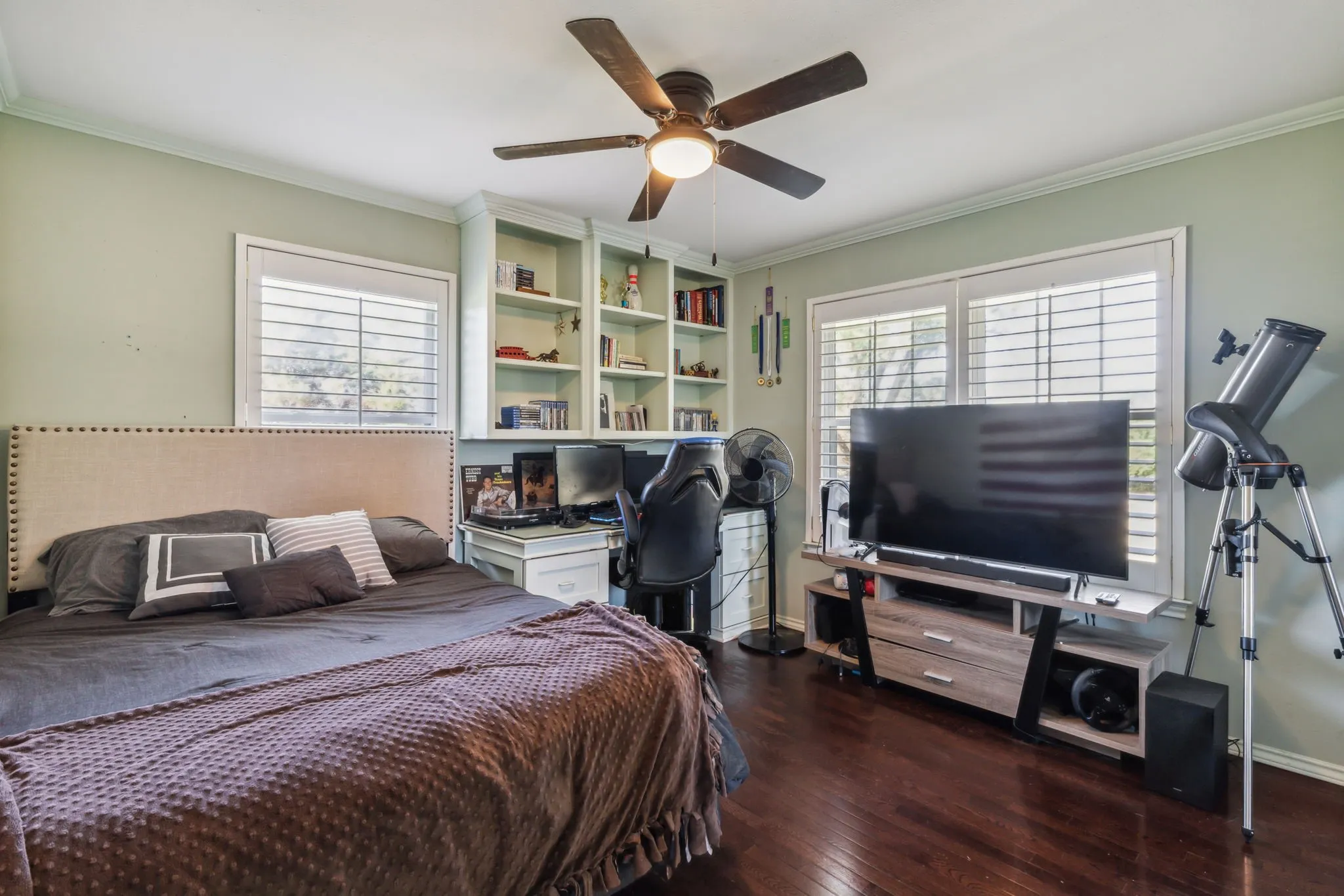 Spacious room featuring rich wood-finish flooring, a ceiling fan, and crown molding