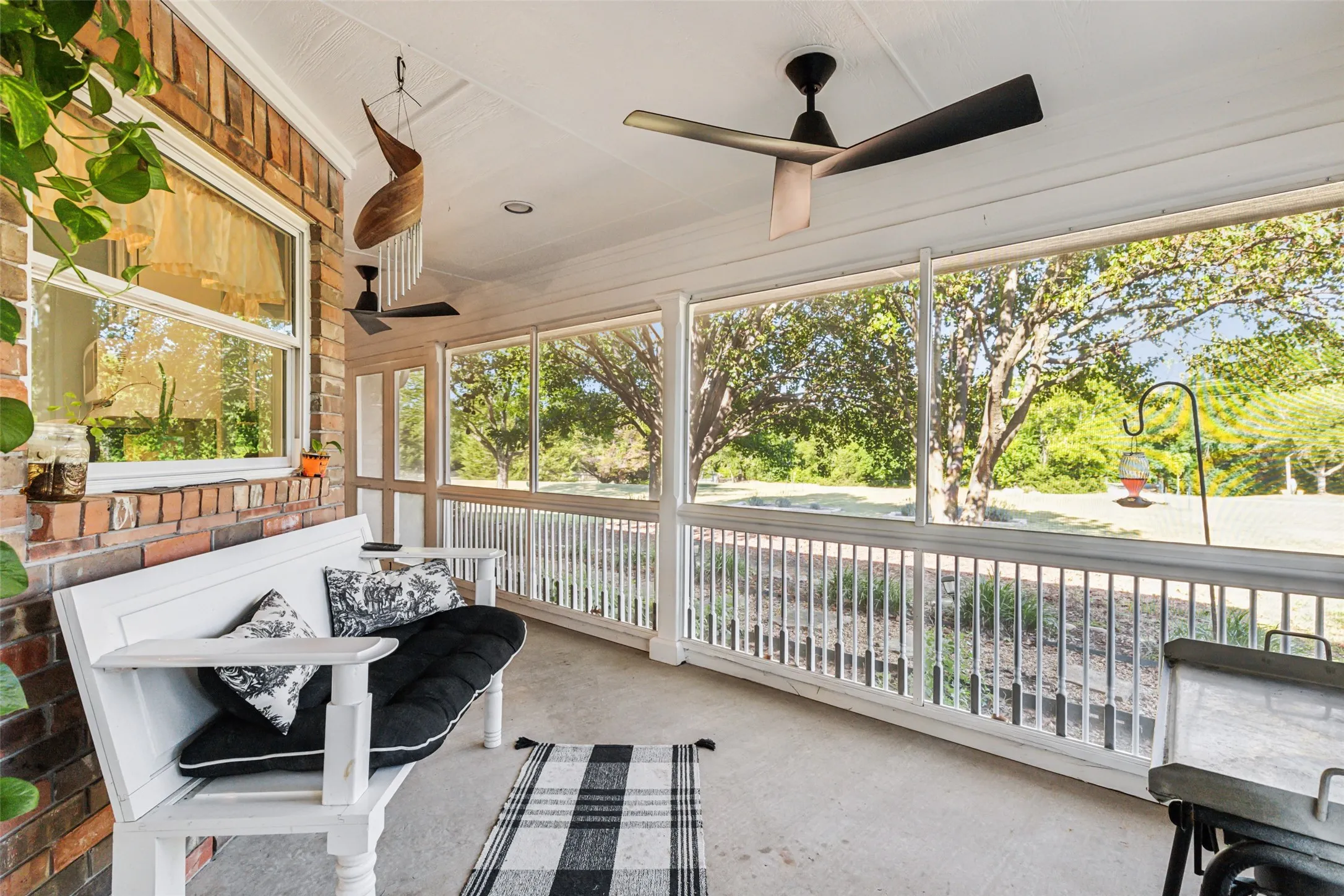 Screened porch with brick exterior wall, concrete flooring, and multiple ceiling fans