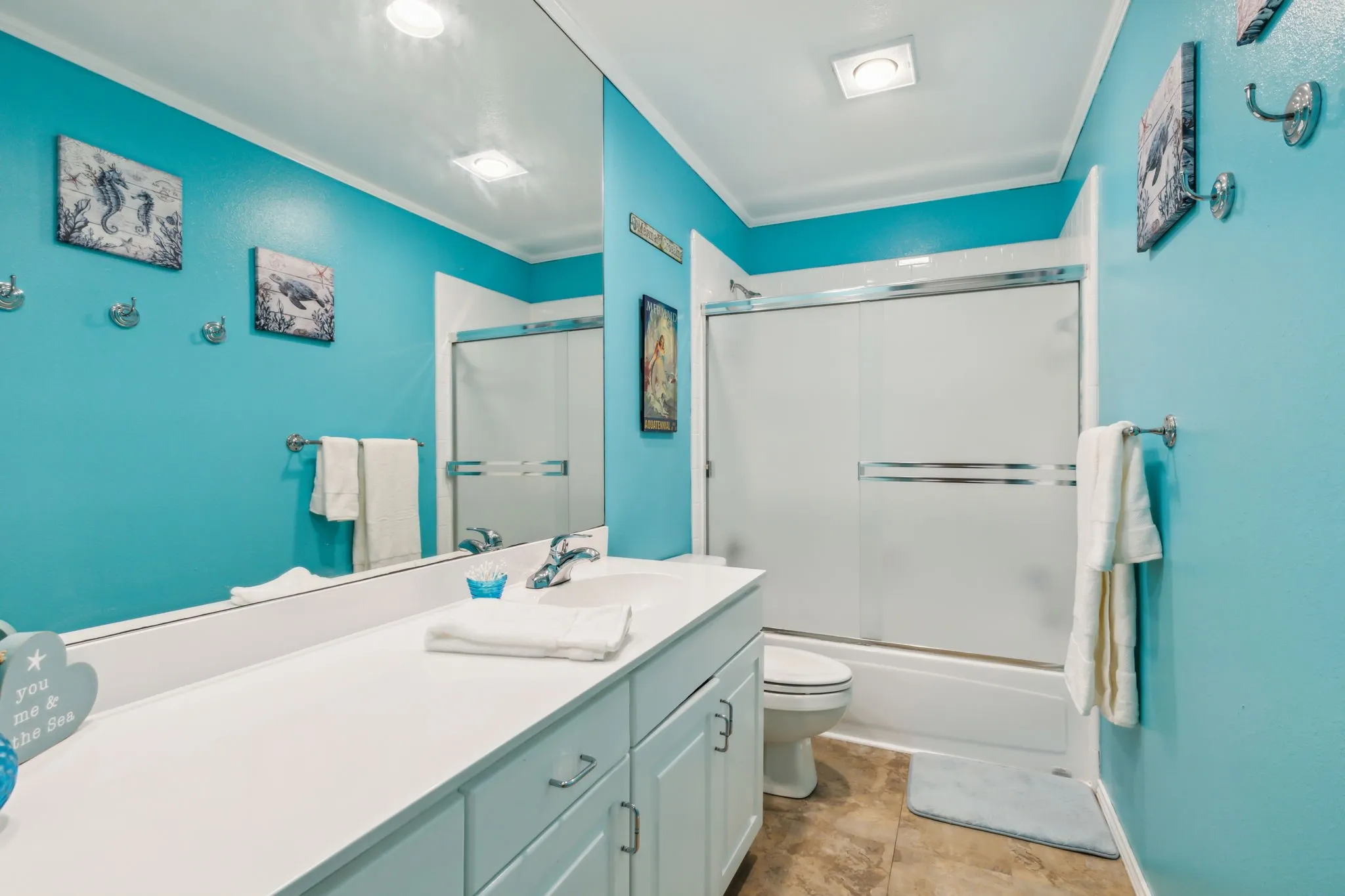 Bathroom featuring a long vanity with a single sink, an integrated mirror, a shower-tub combination with sliding frosted glass doors, and tile flooring