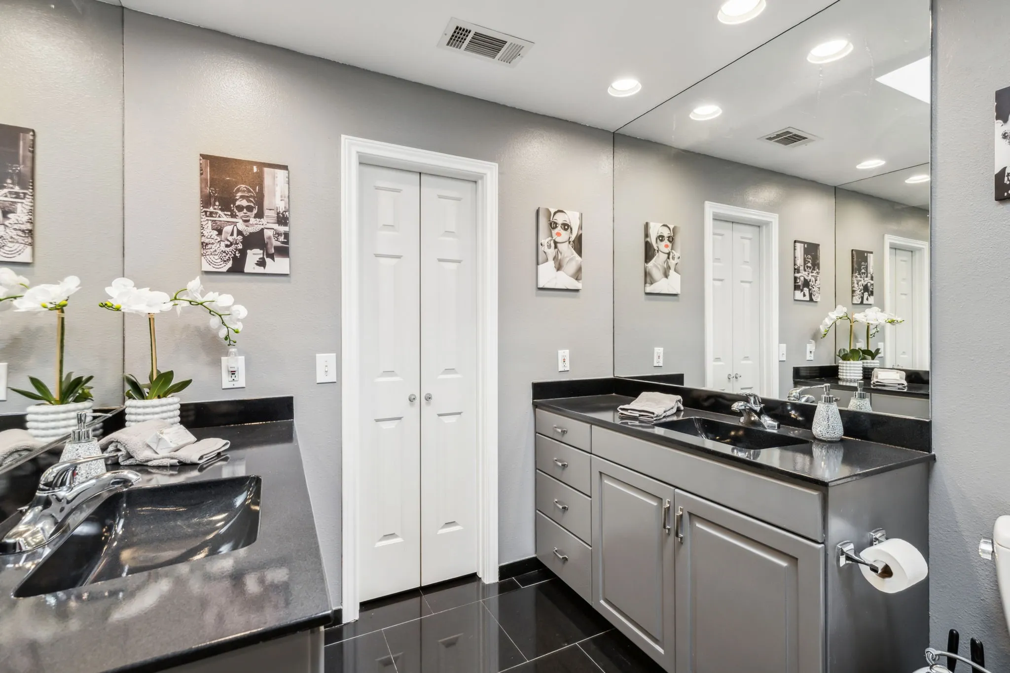 Dual sink vanity featuring a black countertop, integrated black sinks, and gray cabinetry with brushed nickel hardware