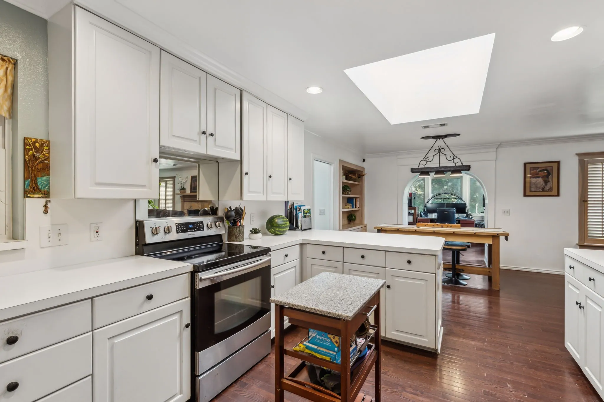 White cabinetry with black hardware, stainless steel range, white countertops, wood-finish flooring, and a ceiling skylight