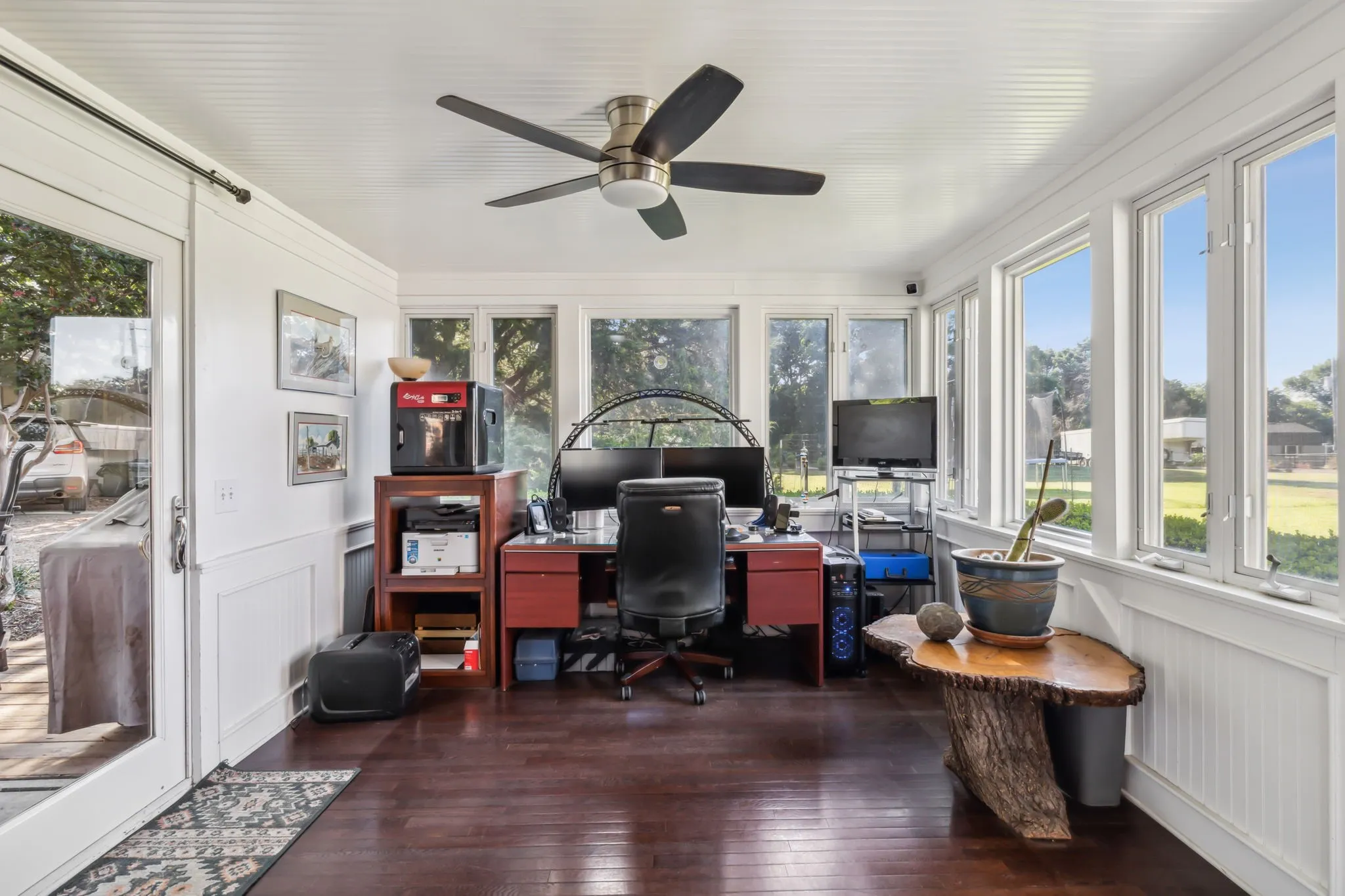 Sun-drenched room featuring dark wood-finish flooring, white beadboard wainscoting, and a full wall of windows