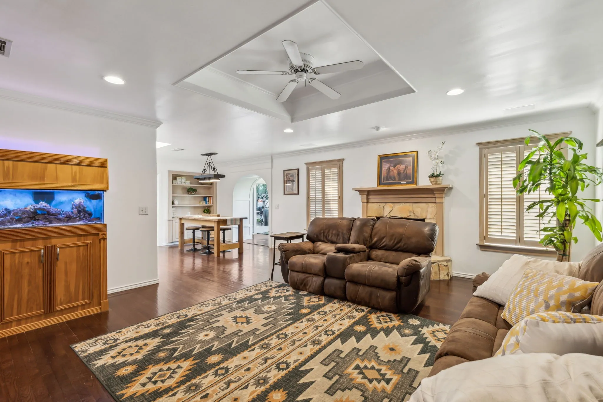 Spacious living area featuring dark wood-finish flooring, a tray ceiling with a ceiling fan, and recessed lighting