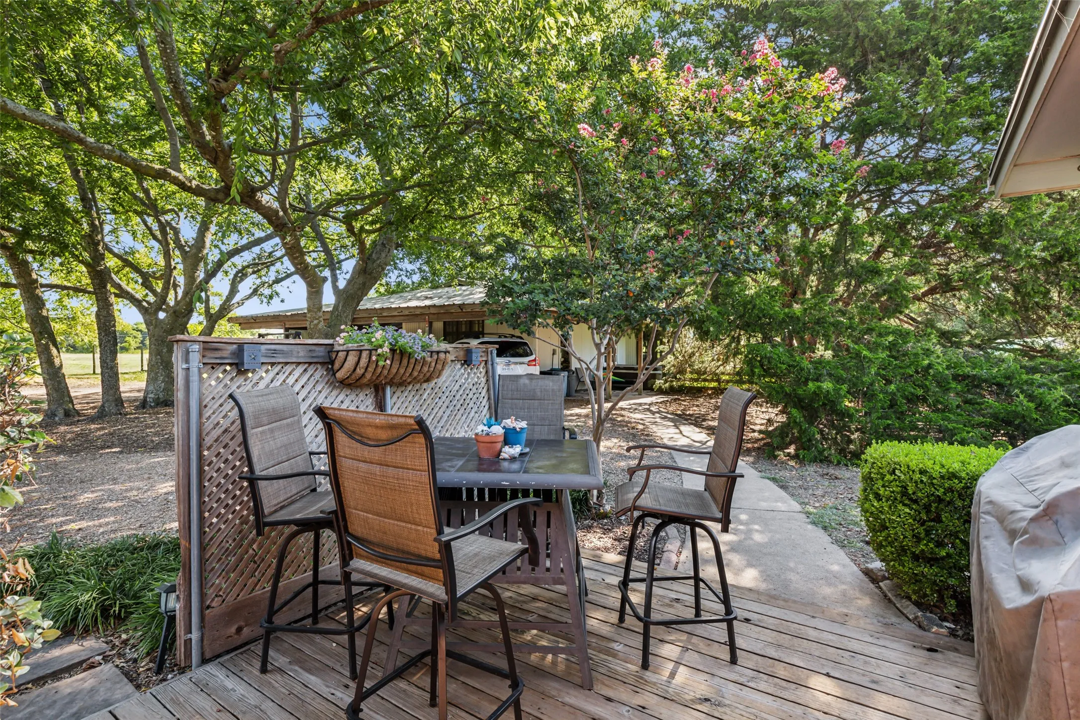 Outdoor wooden deck featuring a lattice privacy screen, mature trees, and landscaping