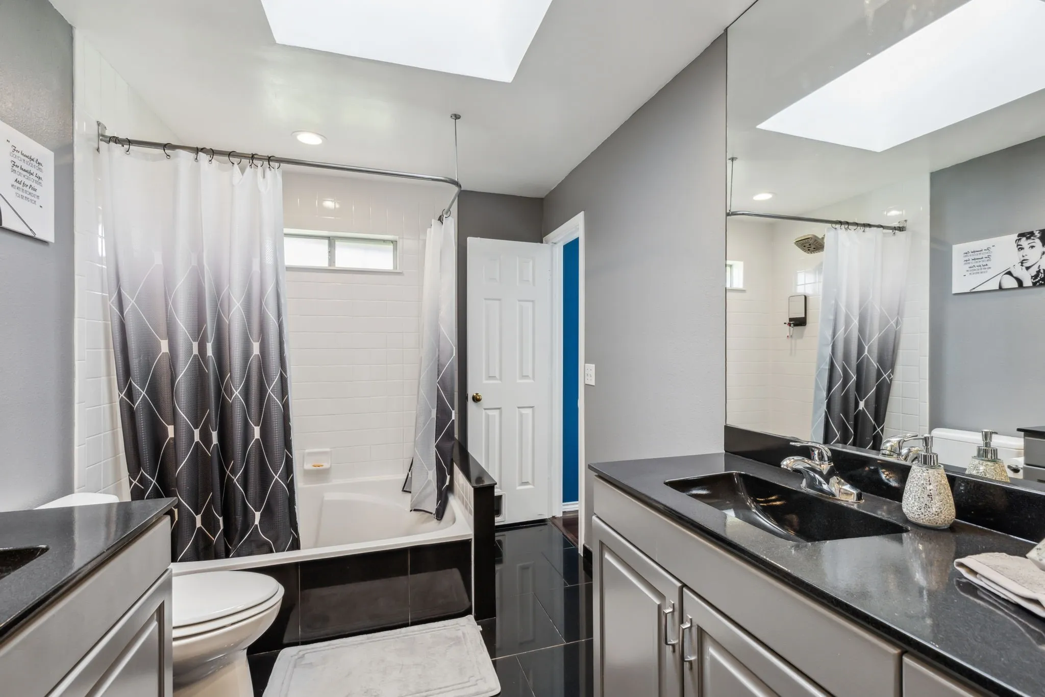 Full bathroom featuring a skylight, a bathtub with white subway tile surround, a dark vanity with integrated sink, and dark tile flooring