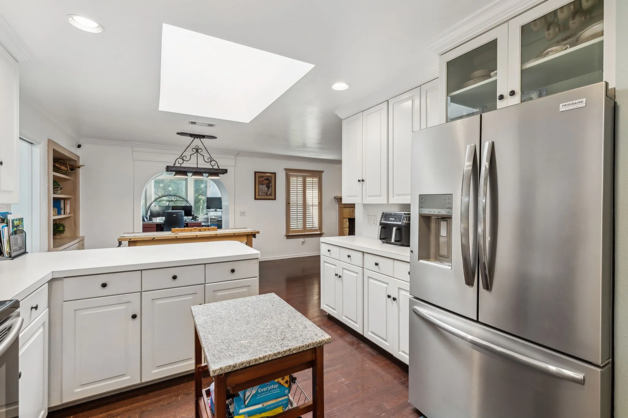 Kitchen featuring white cabinetry, light-toned countertops, hardwood flooring, and a skylight