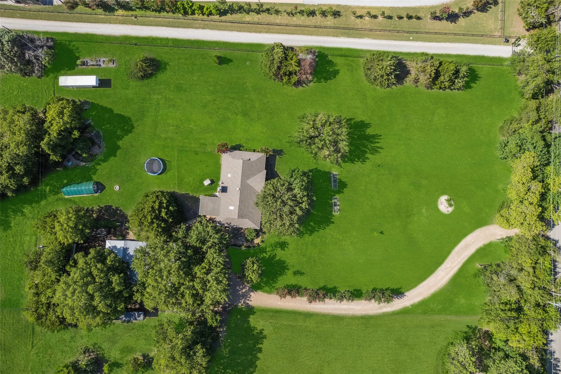 Expansive green property featuring a main residence with a gabled roof, an additional outbuilding, mature trees, and a winding gravel path