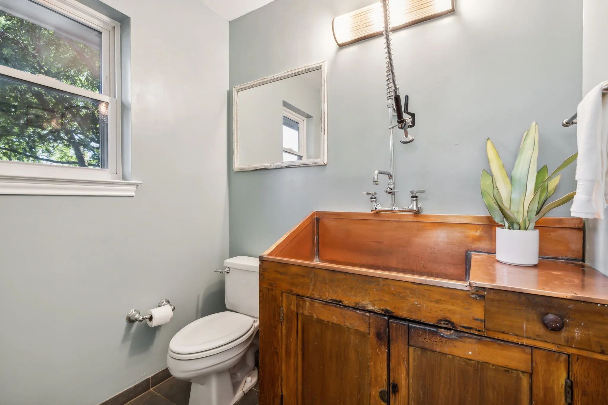 Custom wood vanity with an integrated copper sink, complemented by a wall-mounted faucet with a pull-down sprayer, and a rectangular framed mirror