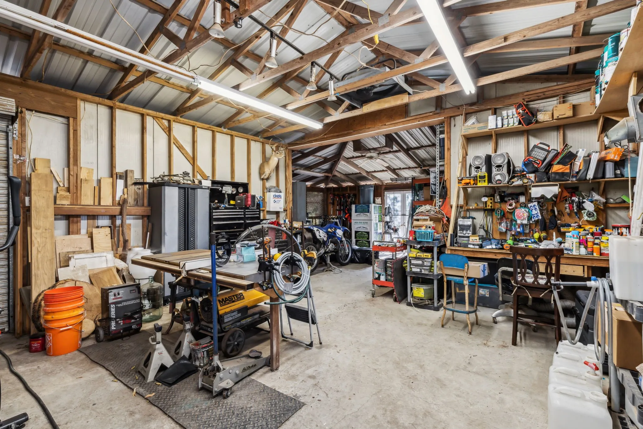 Spacious utility building featuring exposed wood framing, a metal roof, and multiple fluorescent lighting fixtures