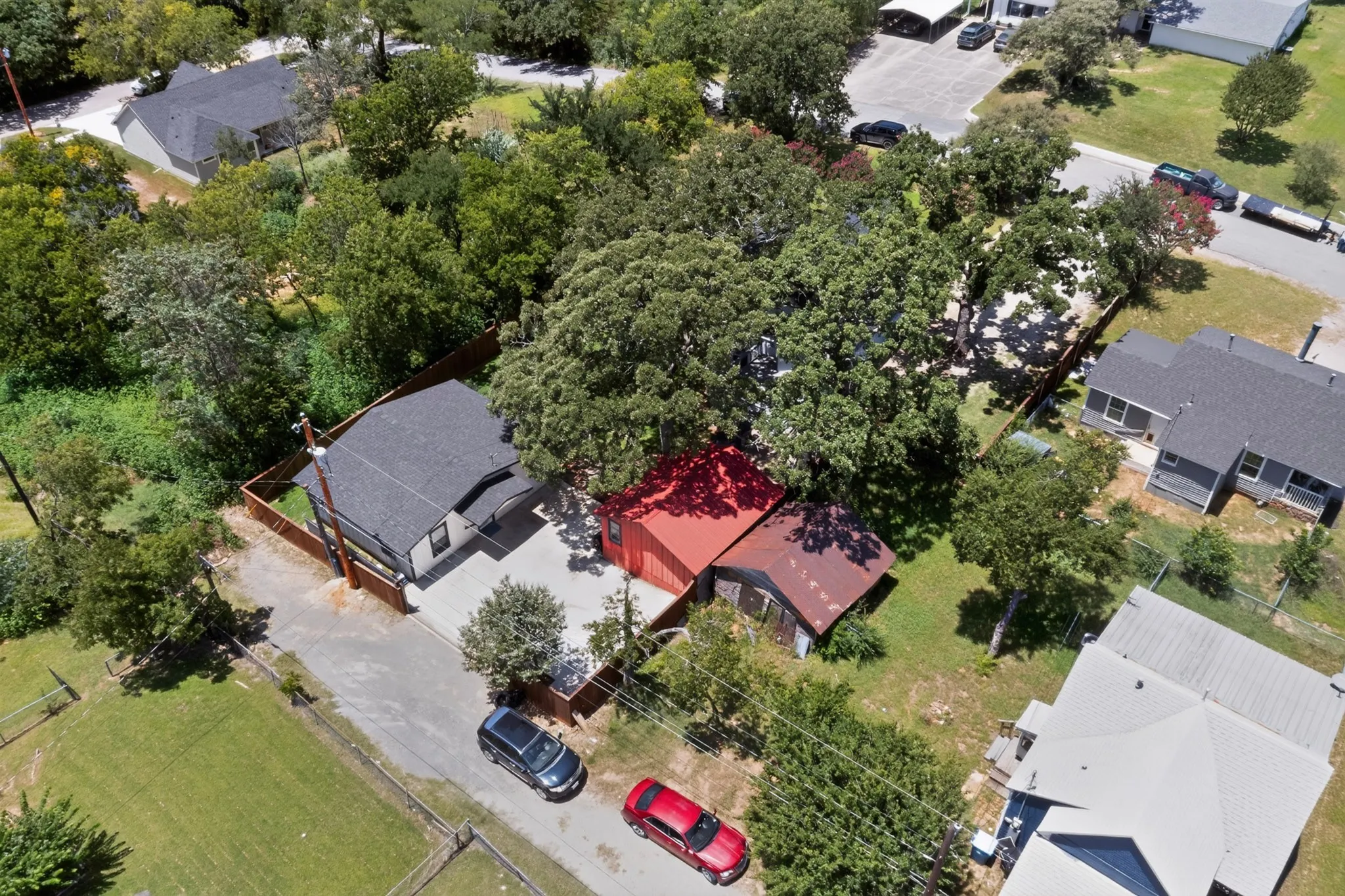 Aerial property overview featuring a dark-shingled roof, light-colored siding, and a paved driveway