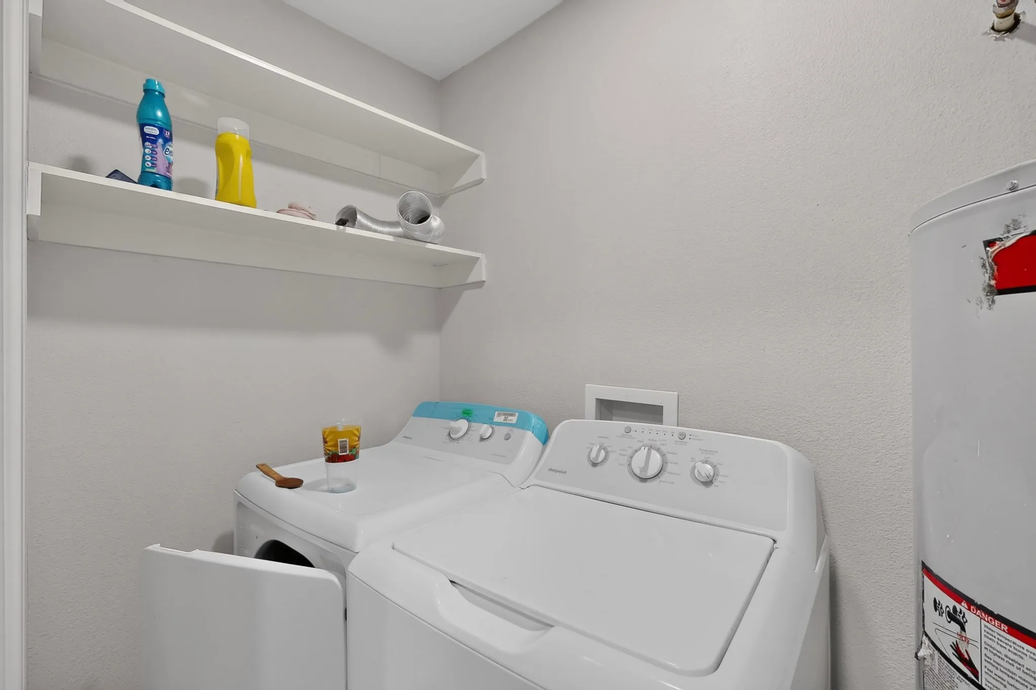 Dedicated laundry area featuring white shelving units, light-colored walls, and a visible water heater