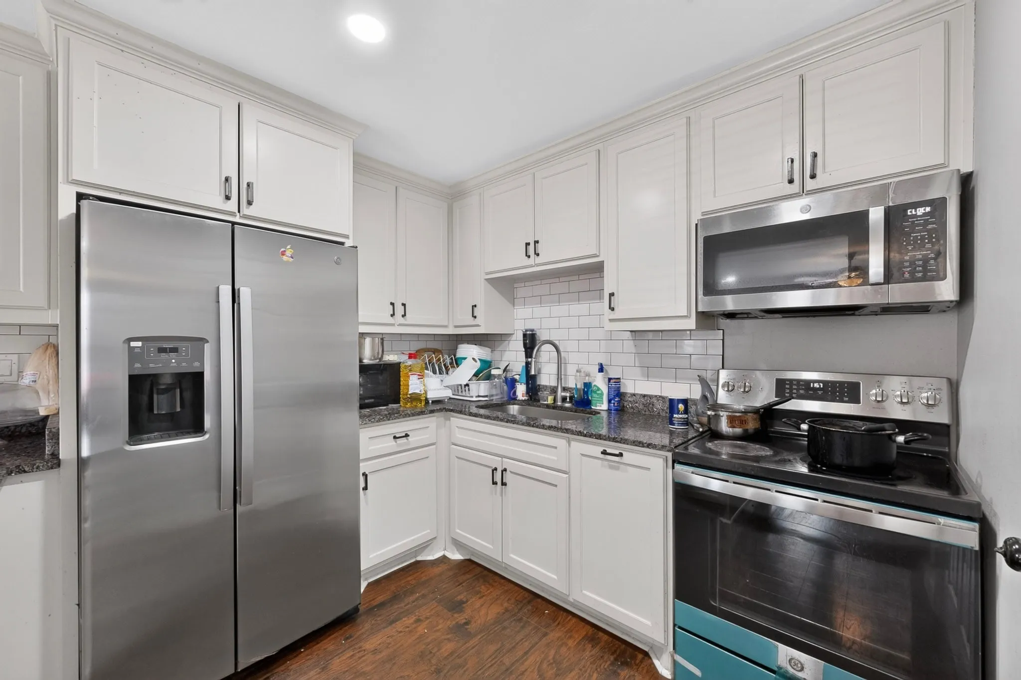 Kitchen featuring white cabinetry, dark speckled countertops, stainless steel appliances including a side-by-side refrigerator, and wood-finish flooring