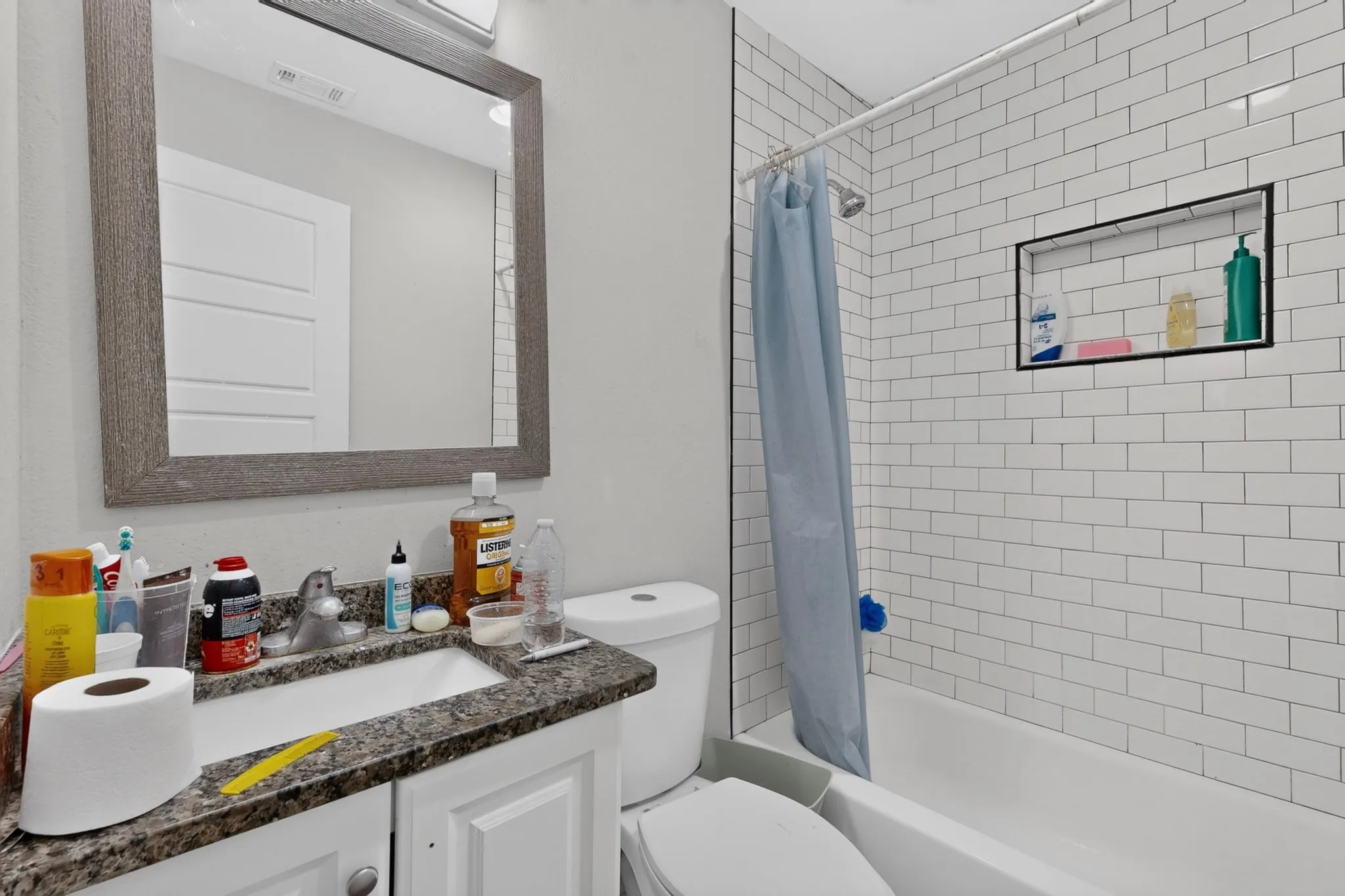 Bathroom featuring a subway tile shower surround with an integrated niche, a white tub, and a vanity with a granite-finish countertop and a single basin sink