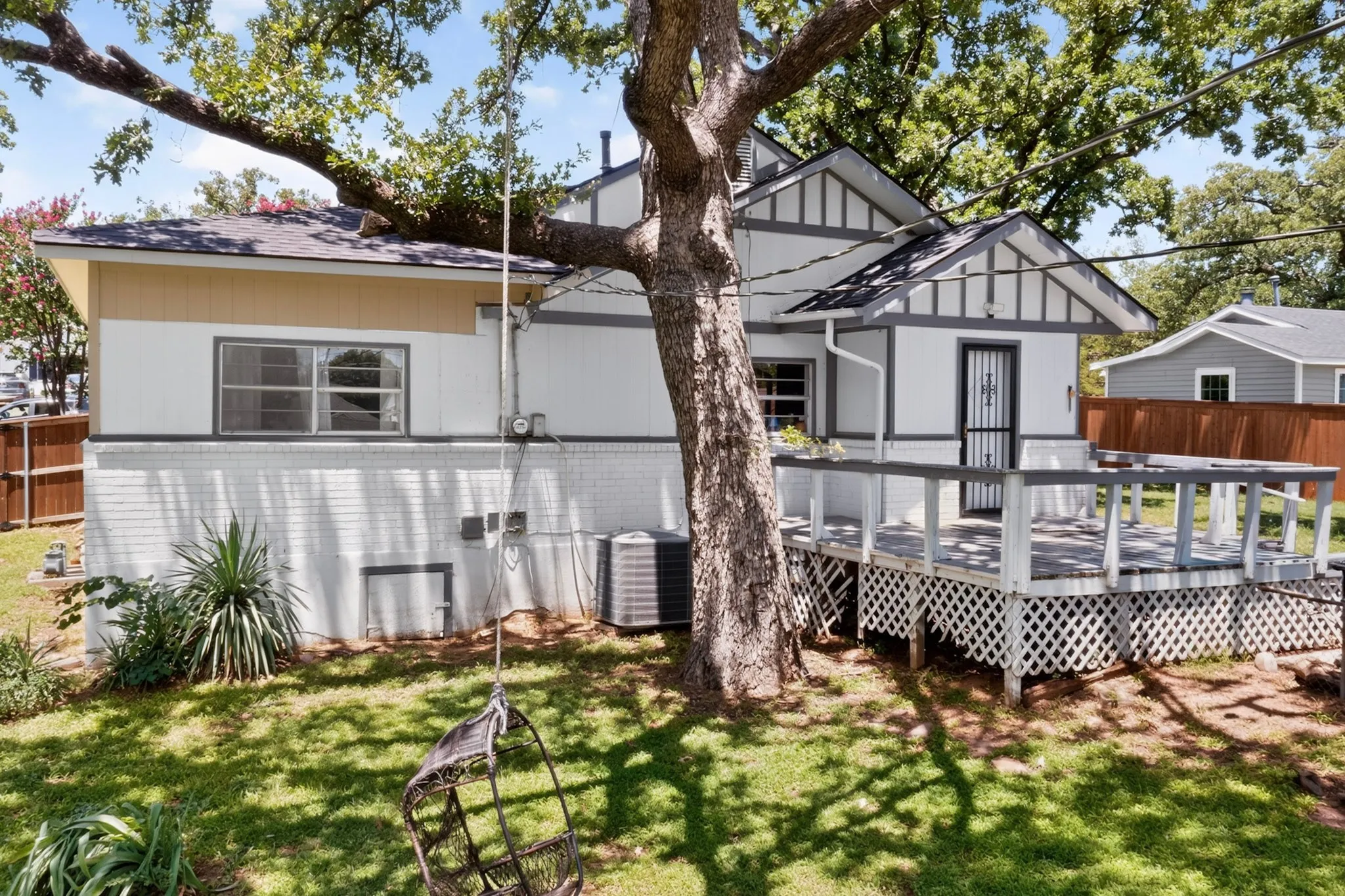 Rear exterior featuring a spacious wooden deck with lattice skirting, mature trees, and a white brick foundation