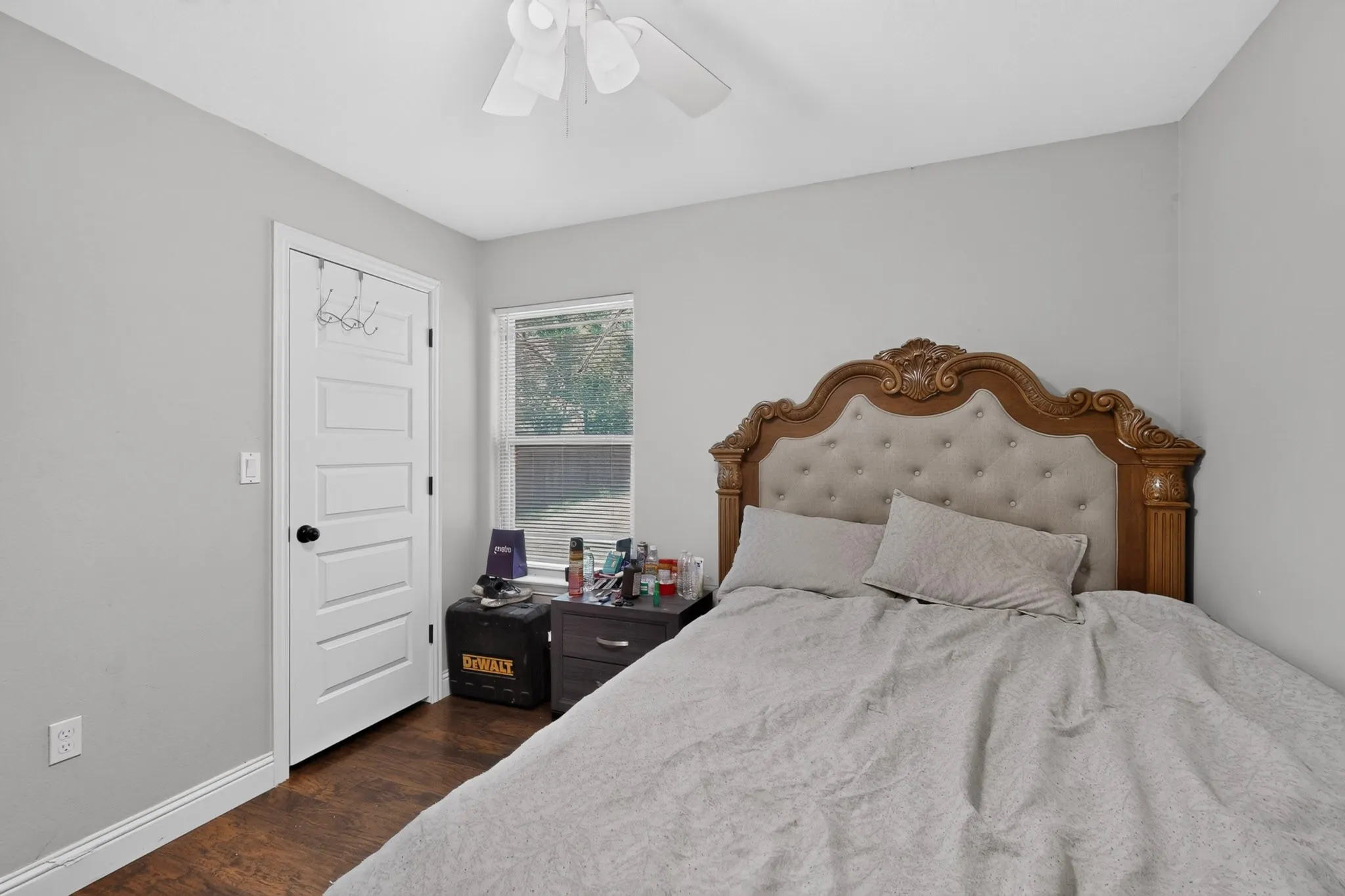 Bedroom featuring light gray walls, wood-finish flooring, a white five-panel door with black hardware, and a window with a natural outdoor backdrop