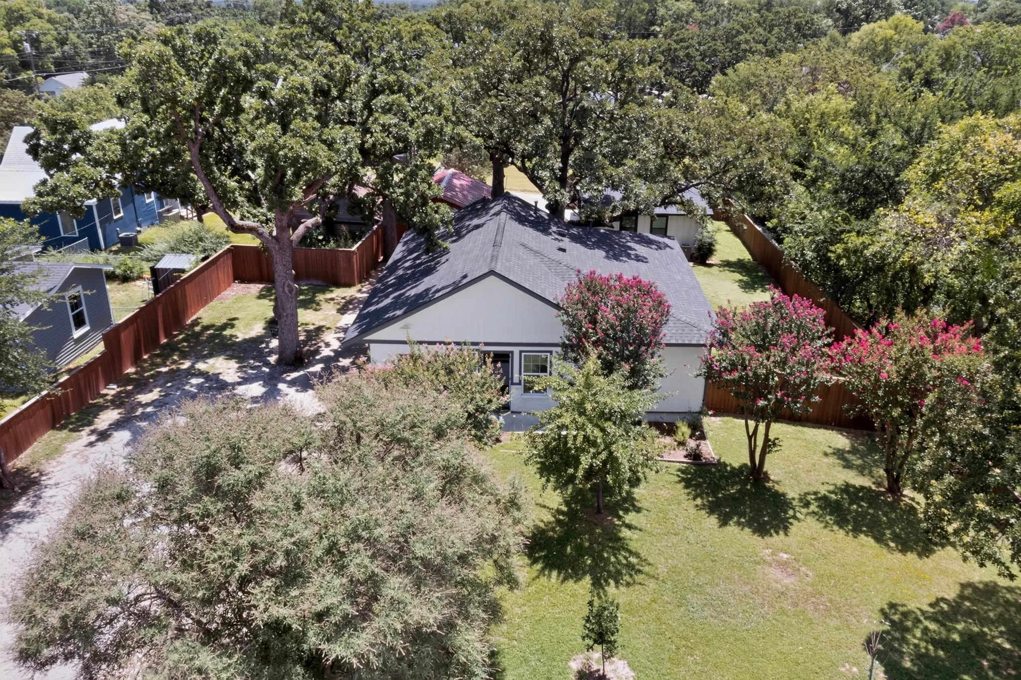 Single-story residence featuring a dark shingle roof, light-toned siding, and a prominent front yard with mature trees