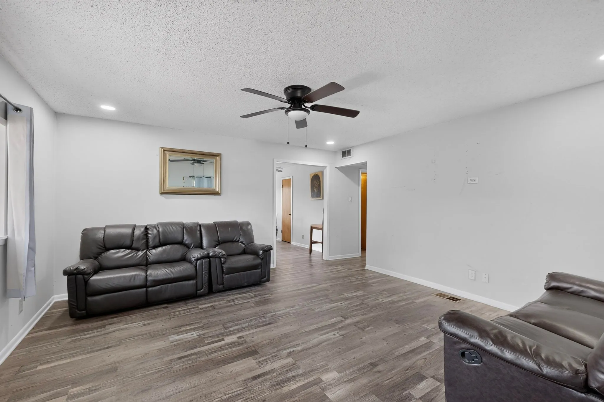 Spacious living area featuring wood-finish flooring, recessed lighting, and a dark-toned ceiling fan
