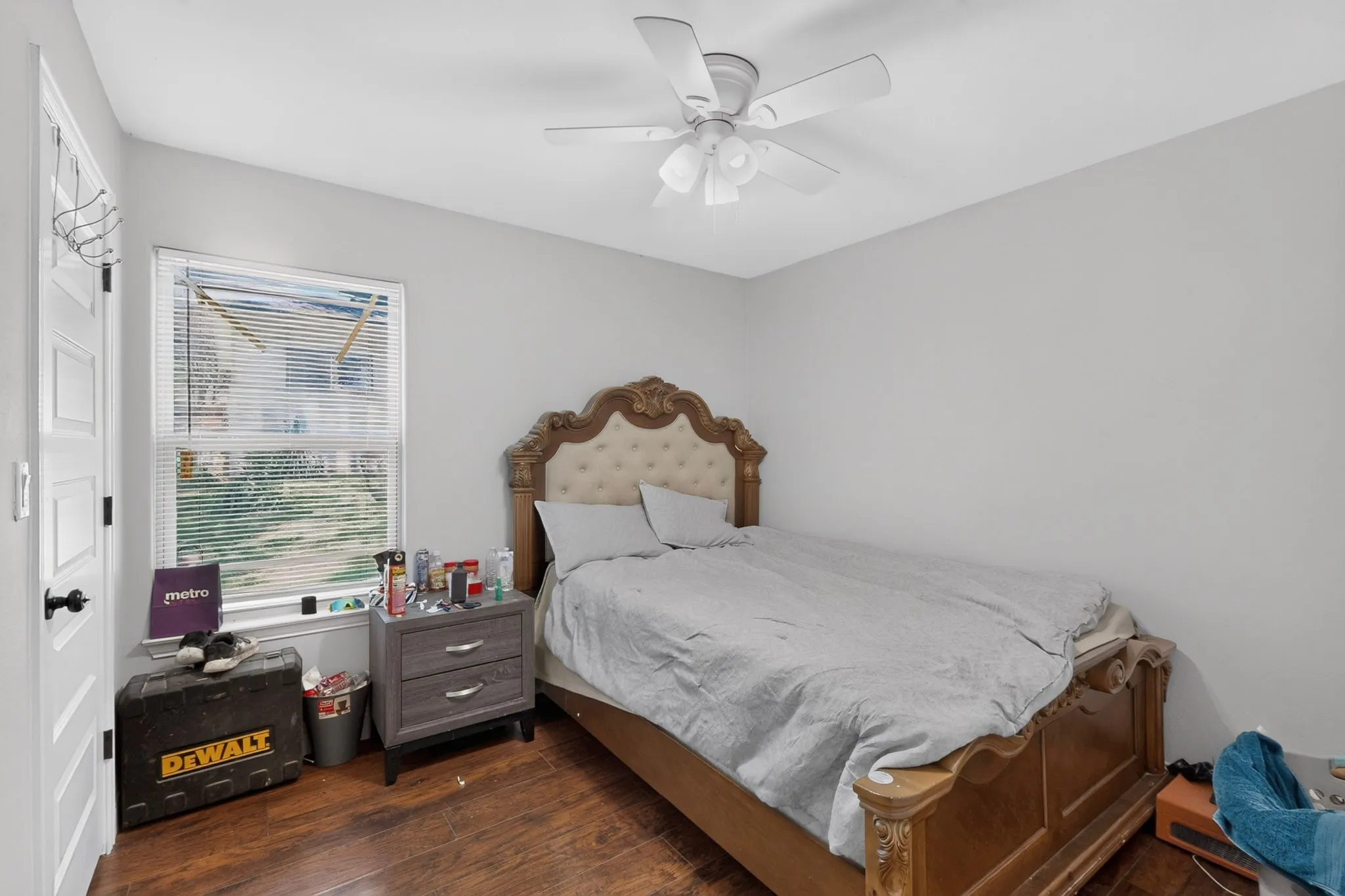 Bedroom featuring wood-finish flooring, a window with blinds, a ceiling fan, white paneled door, and neutral wall paint