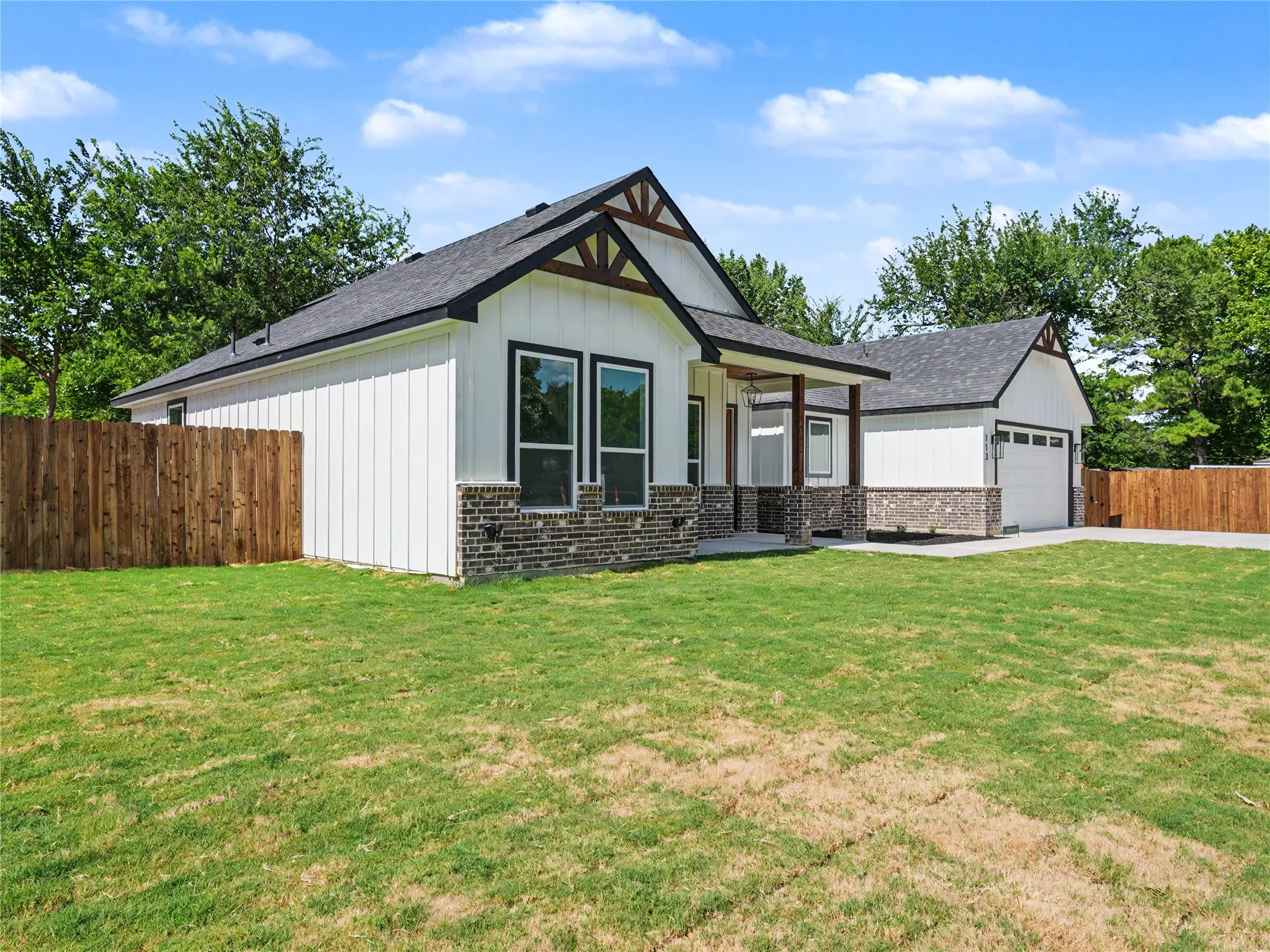 Modern farmhouse exterior featuring white vertical siding, dark brick accents, and a covered porch