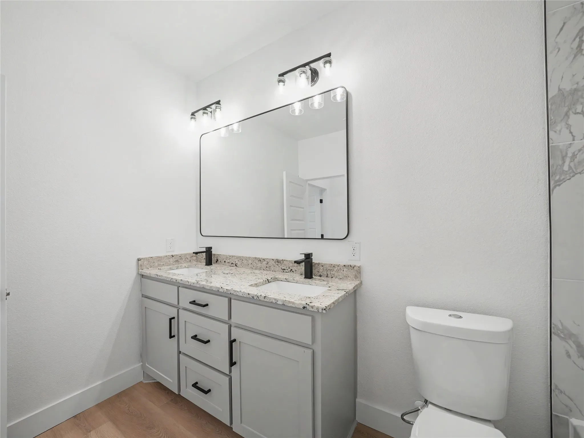 Bathroom featuring a double vanity with light gray cabinetry, speckled countertops, and matte black fixtures