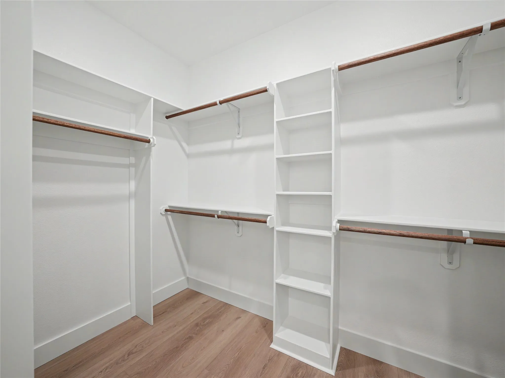 Walk-in closet featuring built-in shelving, multiple hanging rods, white walls, and wood-finish flooring