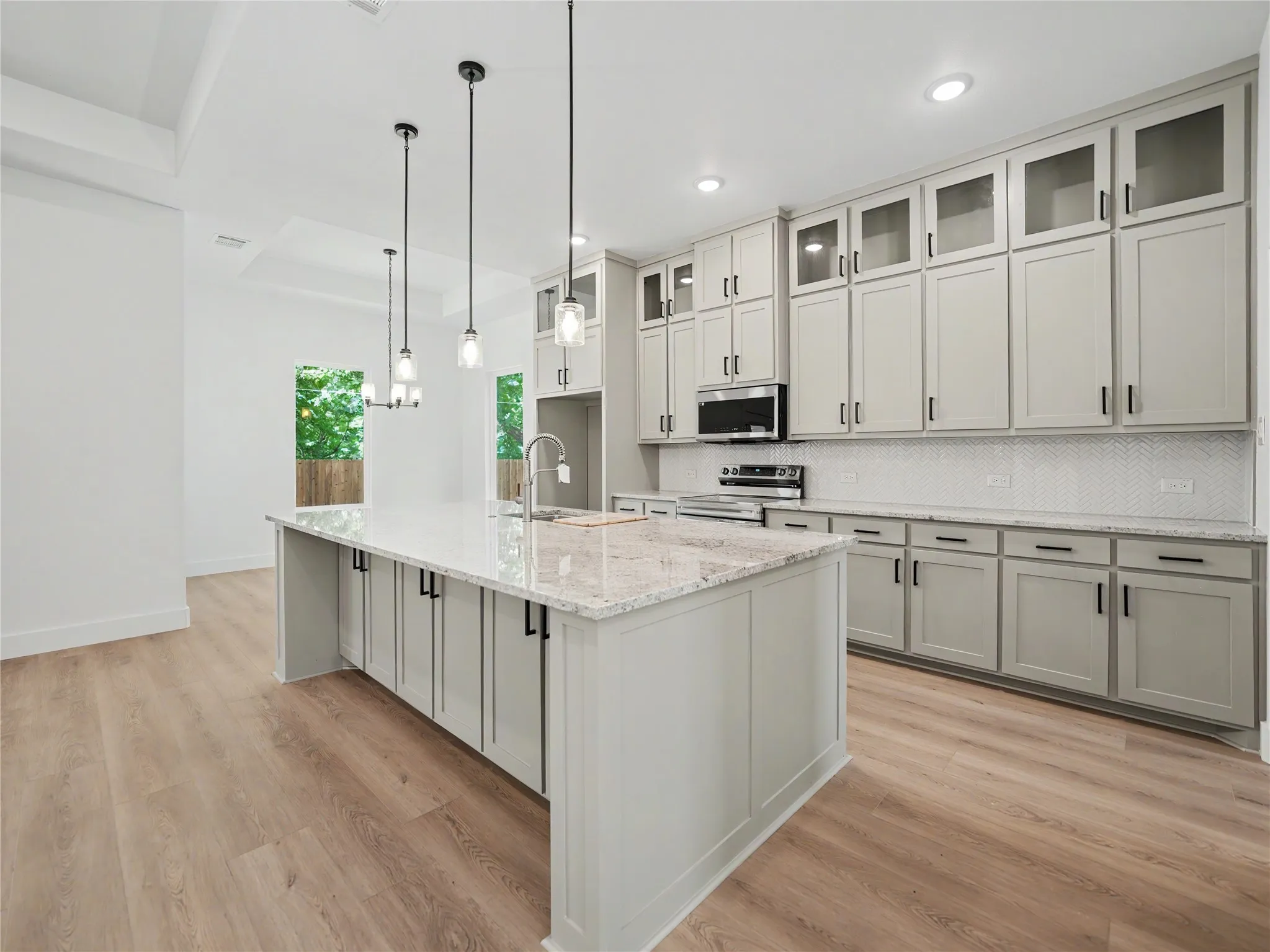 Gourmet kitchen featuring a large island, light-toned cabinetry, granite countertops, wood-finish flooring, and pendant lighting