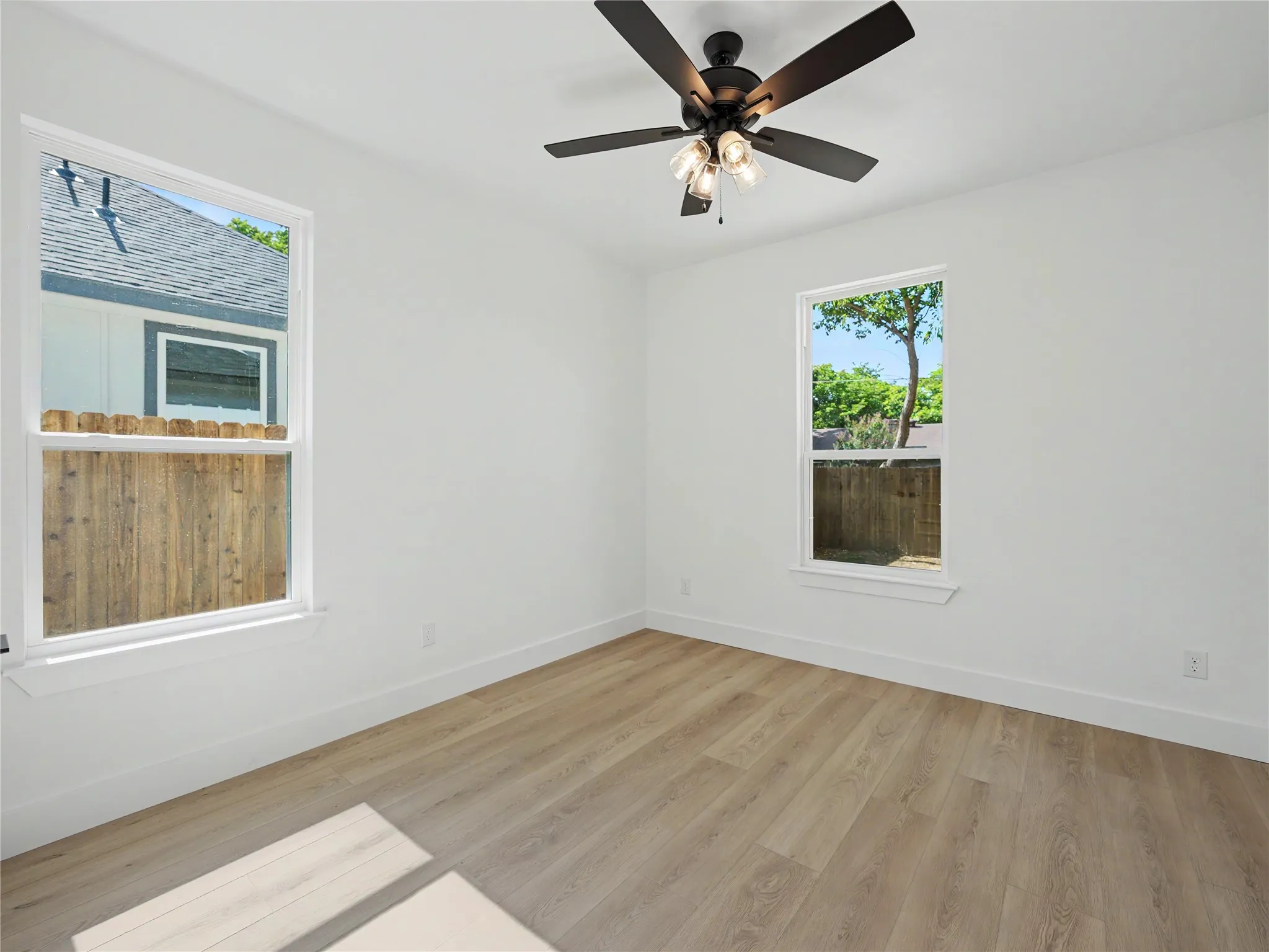 Room featuring wood-finish flooring, white walls, and a ceiling fan with light fixture