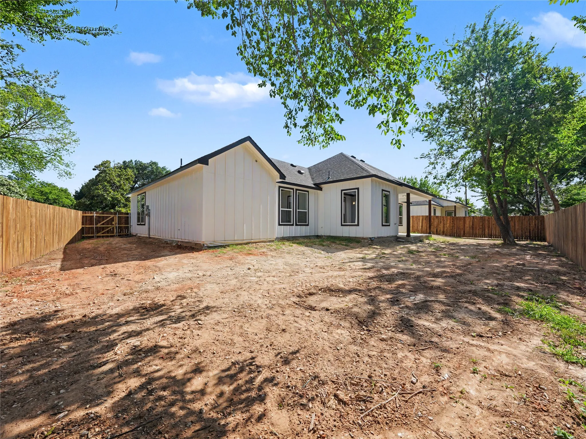 Spacious backyard featuring a newly installed wooden privacy fence, a covered patio area, and a white board-and-batten exterior with contrasting dark trim windows