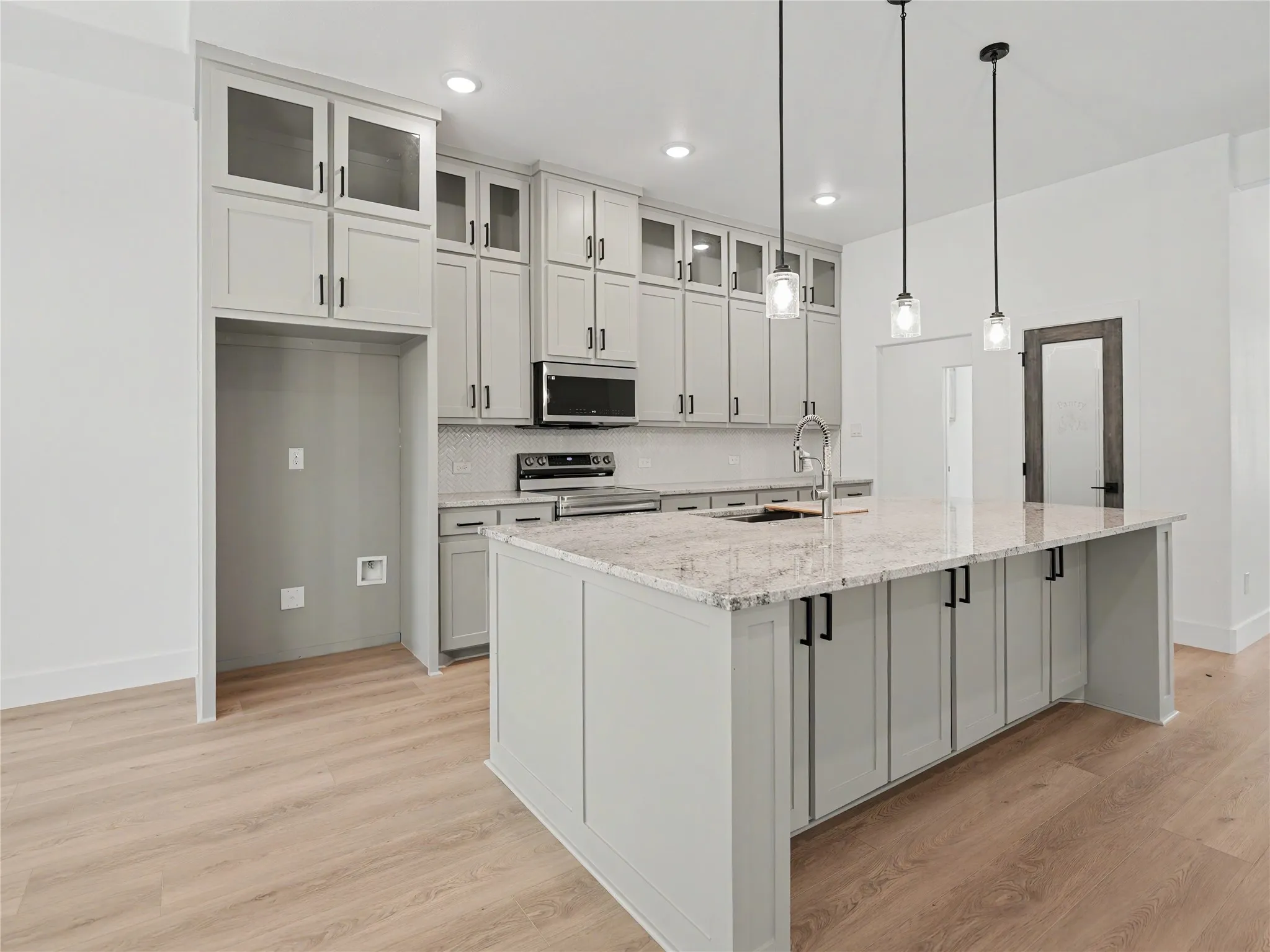 Open-concept kitchen featuring an expansive central island with a light-colored countertop, light gray cabinetry, and a subway tile backsplash