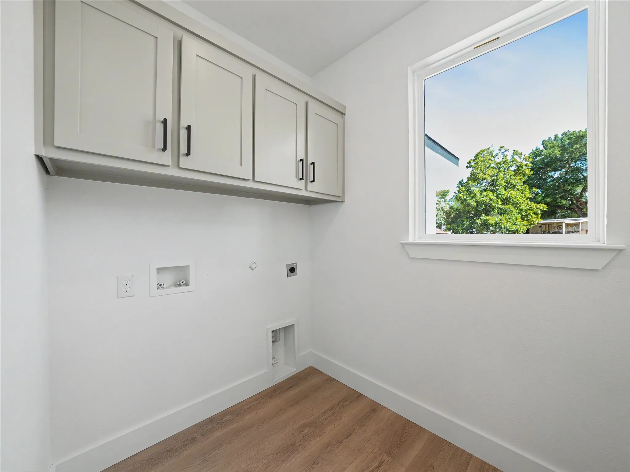 Laundry area featuring wood-finish flooring, white walls, and a window with a white frame