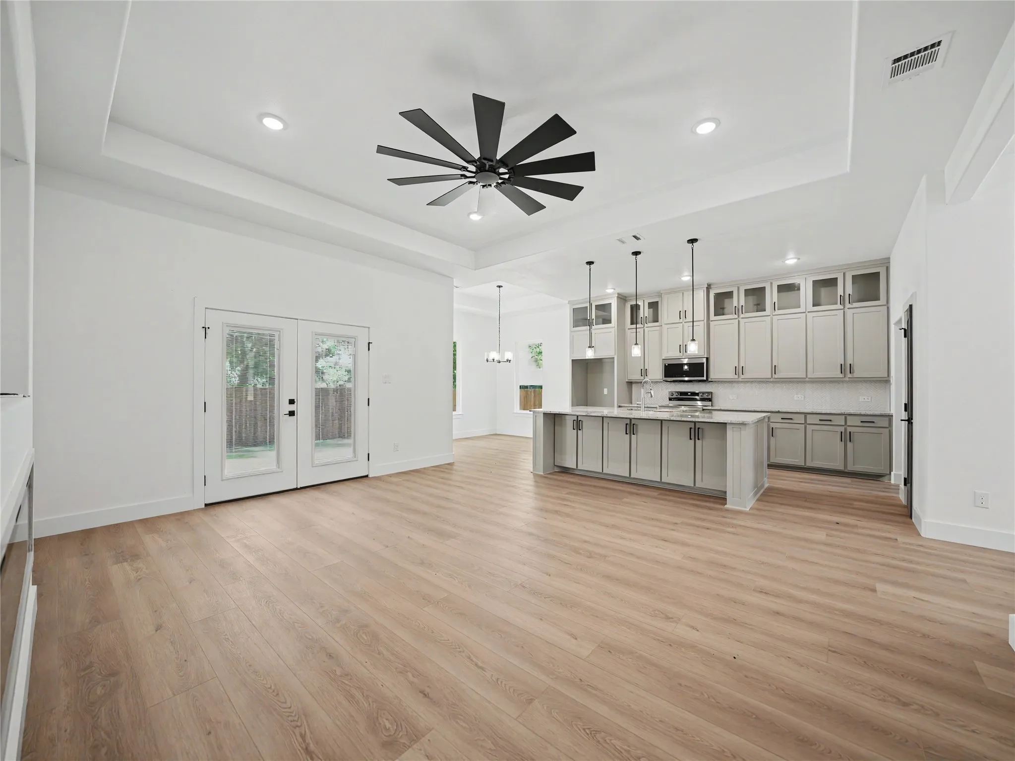 Open-concept living space featuring light wood-finish flooring, a tray ceiling with a contemporary ceiling fan, and recessed lighting