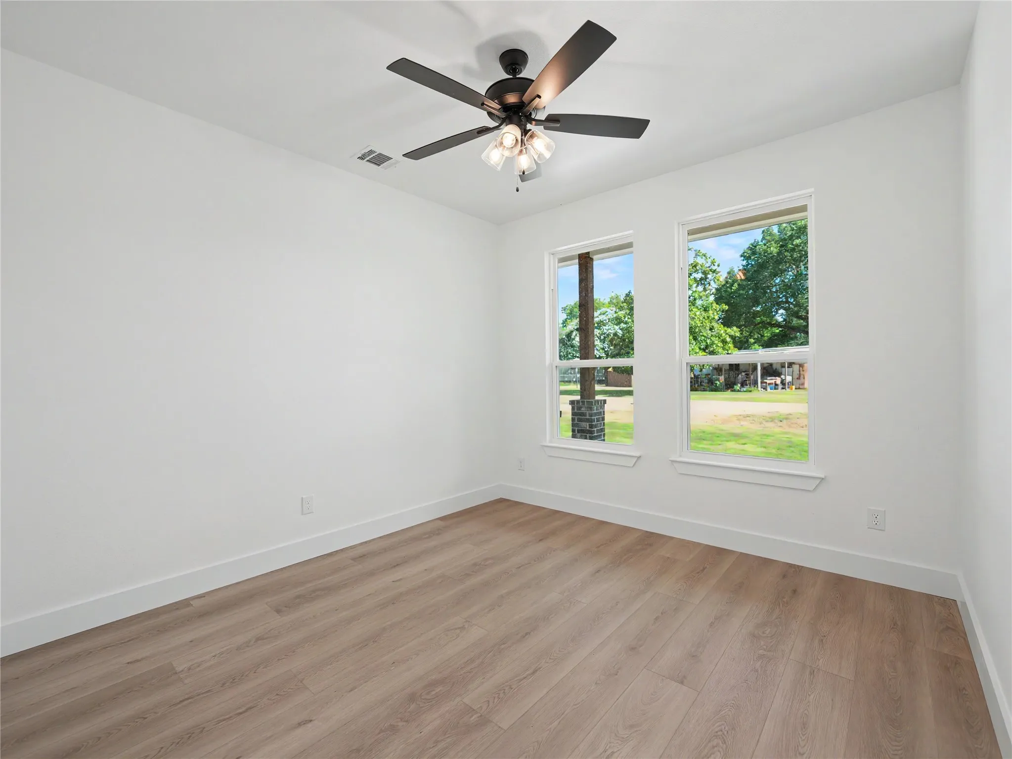 Light-filled interior space featuring two windows, wood-finish flooring, and a ceiling fan with integrated lighting