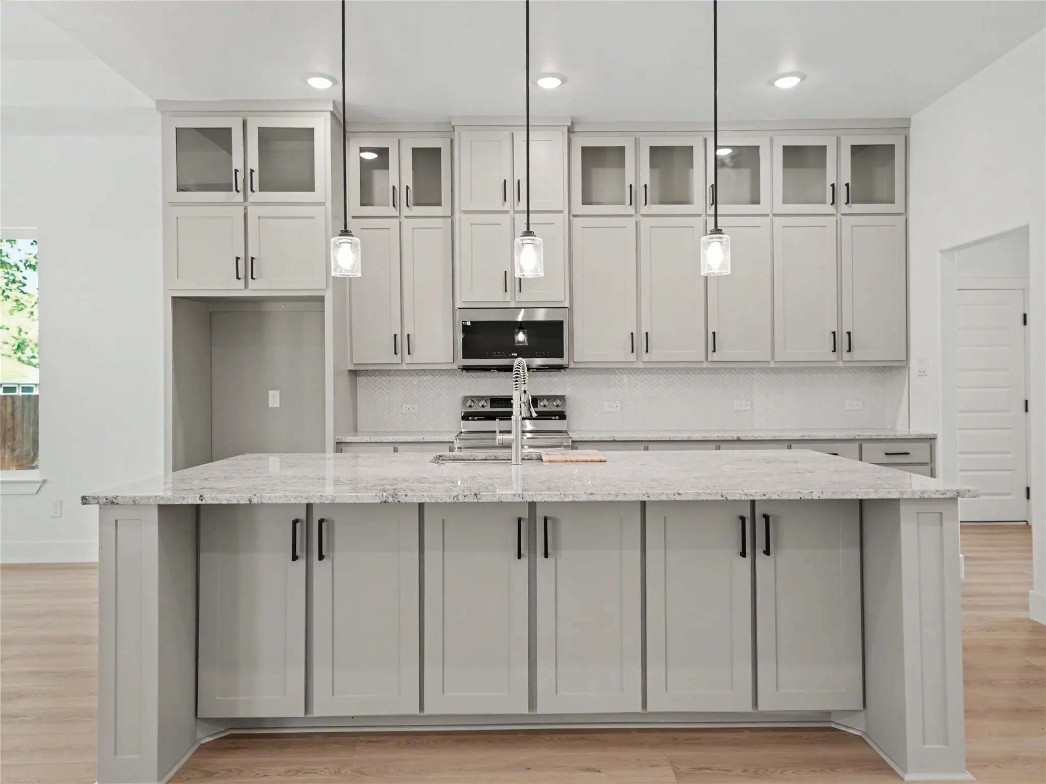 Central kitchen island with a light-toned countertop, shaker-style cabinetry, a built-in sink, and three pendant light fixtures