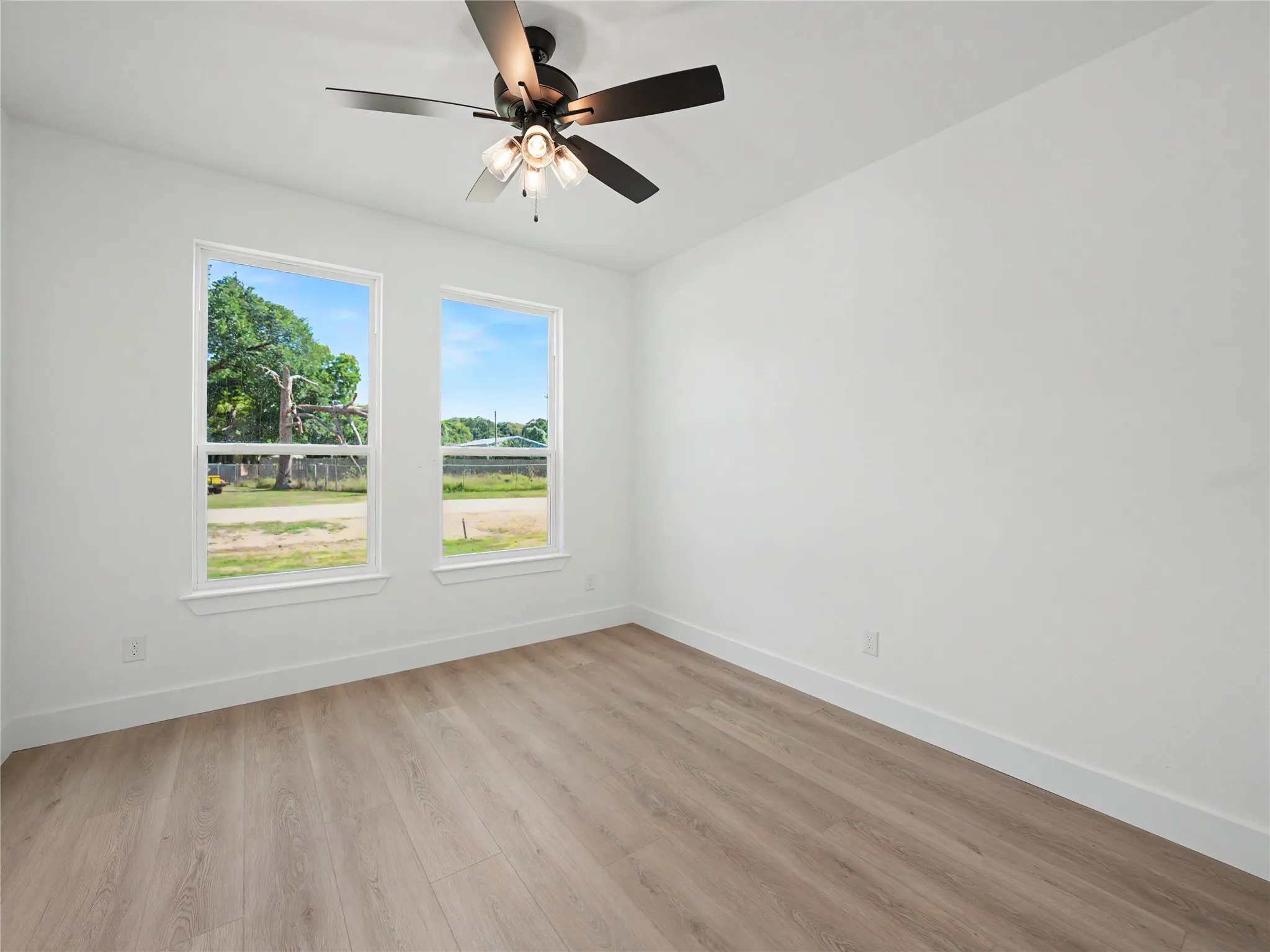 Room featuring wood-finish flooring, white baseboards, and two windows with white trim