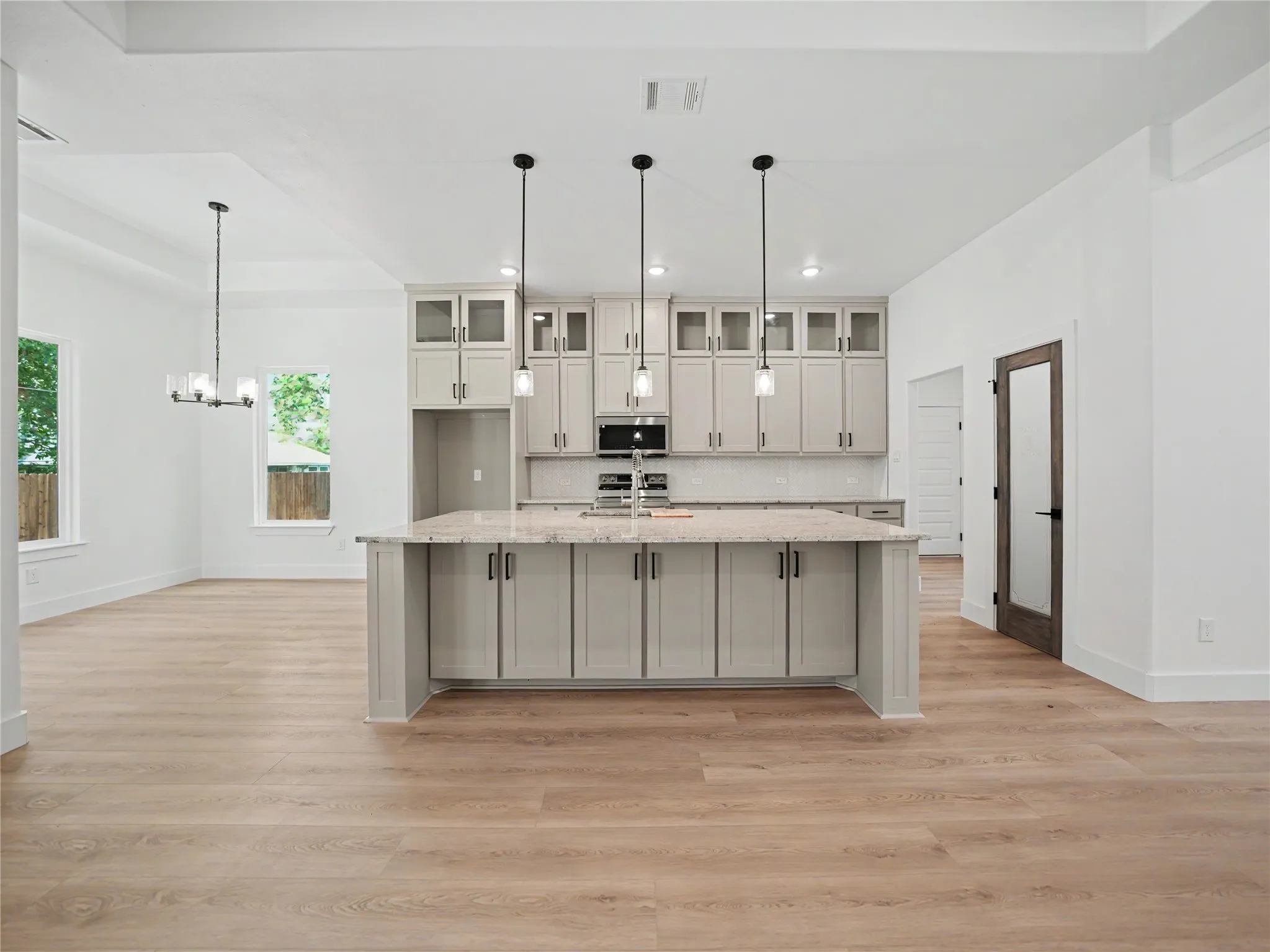 Open-concept kitchen featuring a large central island with a light-toned countertop, grey shaker-style cabinetry, and three pendant lights