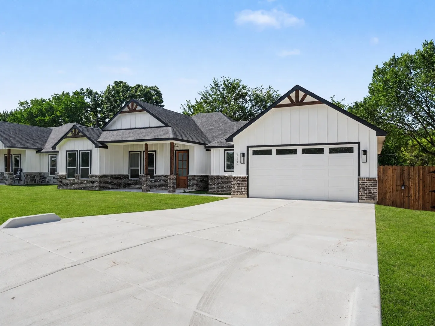 Modern farmhouse exterior featuring white board and batten siding, dark stone accents, and a contrasting dark roof