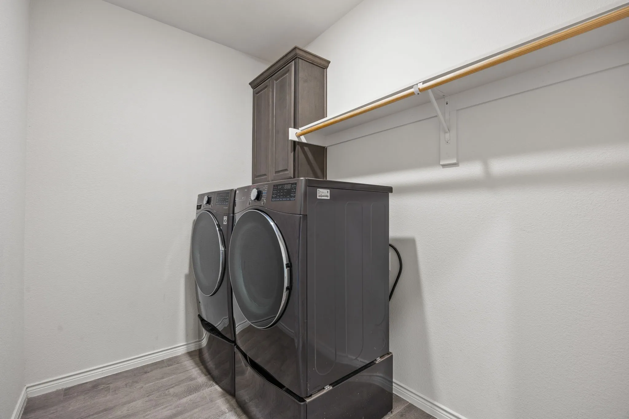 Spacious laundry area featuring wood-finish flooring, white walls, built-in shelving, and an overhead clothes rod