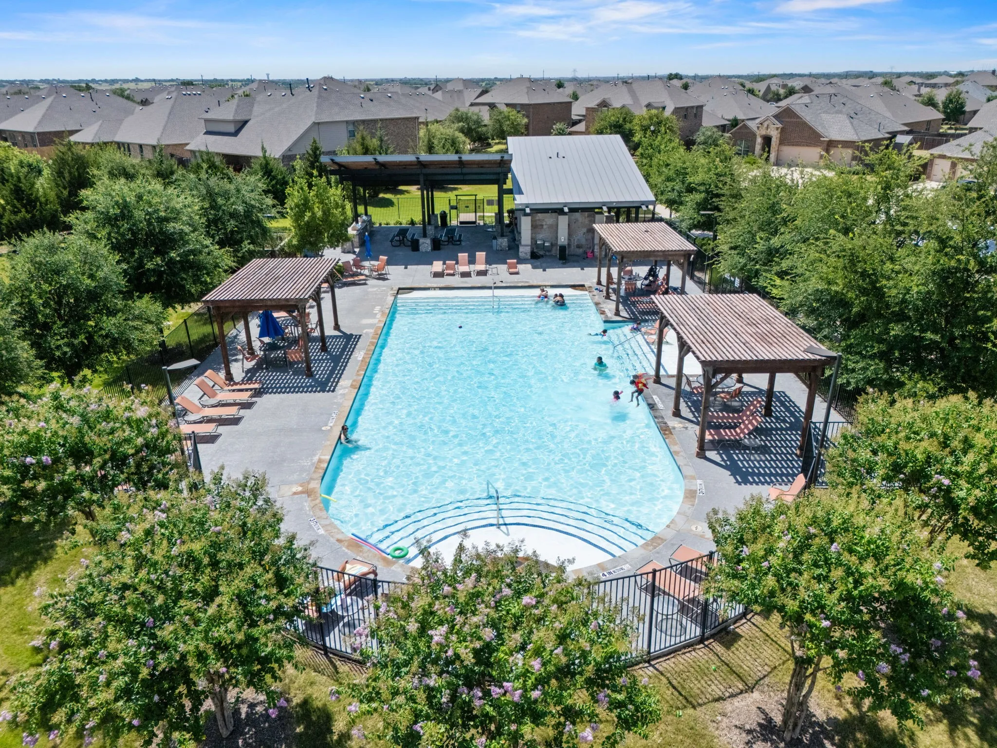 Expansive community swimming pool featuring built-in steps and multiple shaded pergolas