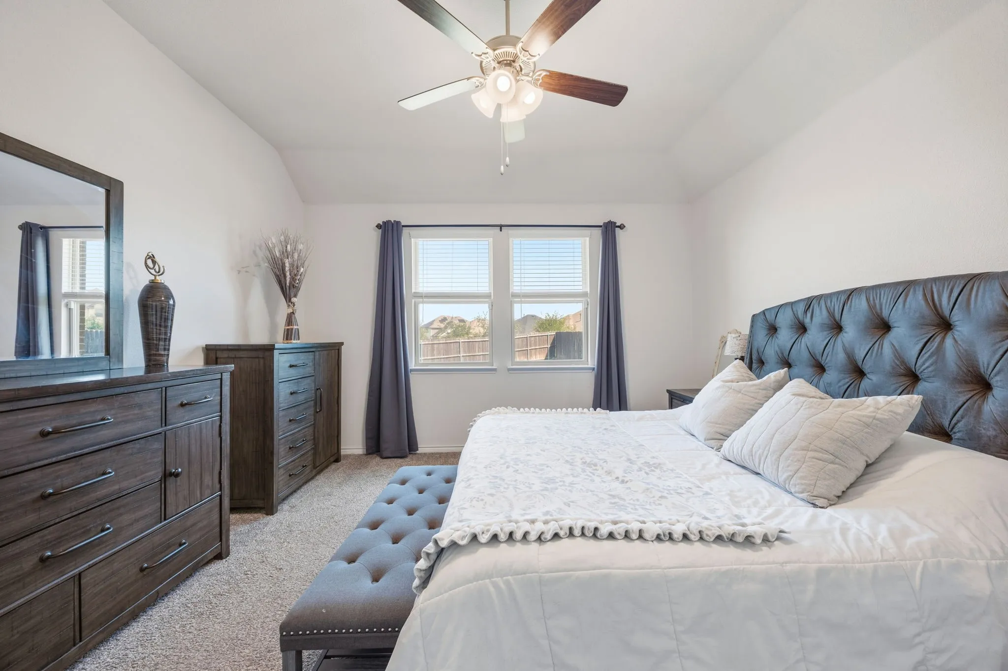 Spacious bedroom featuring vaulted ceilings, a ceiling fan with integrated lighting, and multiple windows with blinds