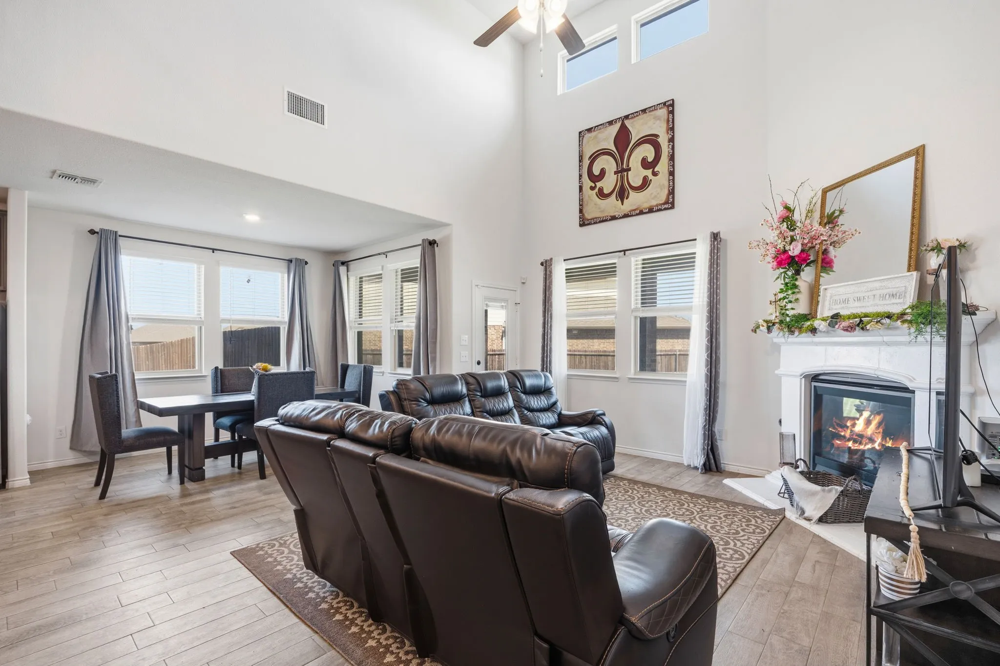 Two-story living area featuring high ceilings, wood-finish tile flooring, a fireplace with a detailed mantel, and multiple windows for natural light