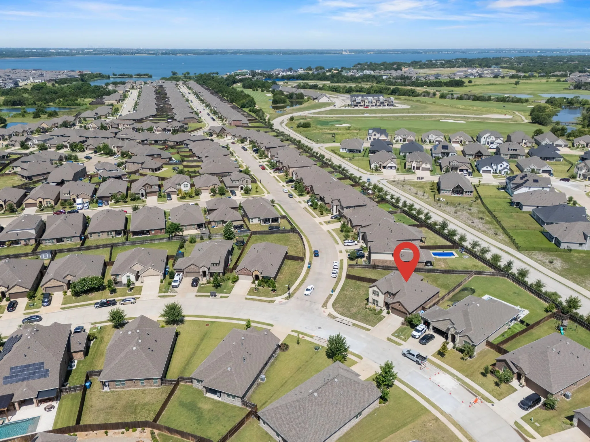 Aerial perspective showcasing a residential community with numerous single-family homes, a prominent body of water in the background, and open green spaces